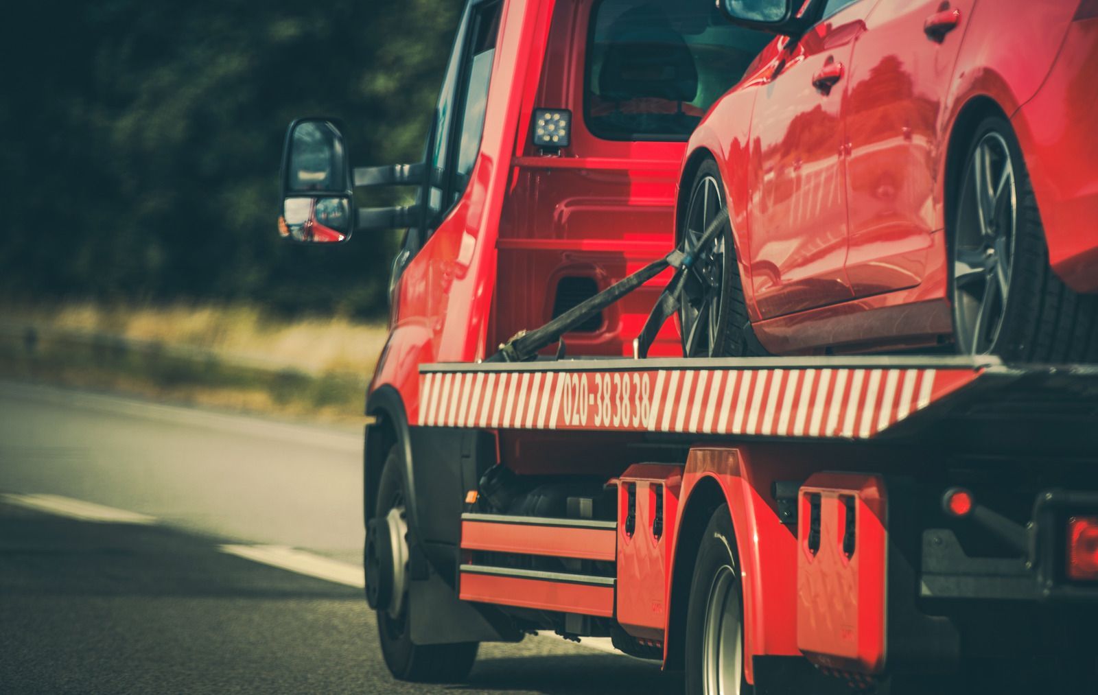 A red tow truck is towing a red car down the road.