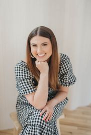 Smiling woman in a black-and-white checkered dress sitting indoors with her chin resting on her hand