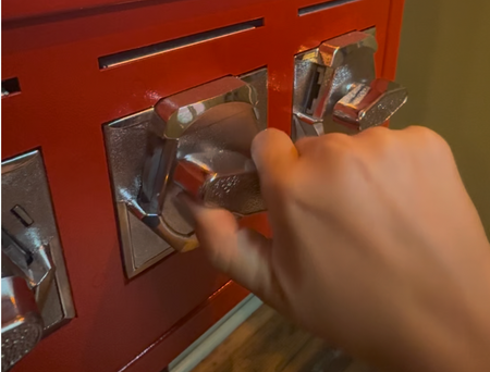 Hand inserting a ballot into a red mail-in ballot drop box with clear plastic flaps
