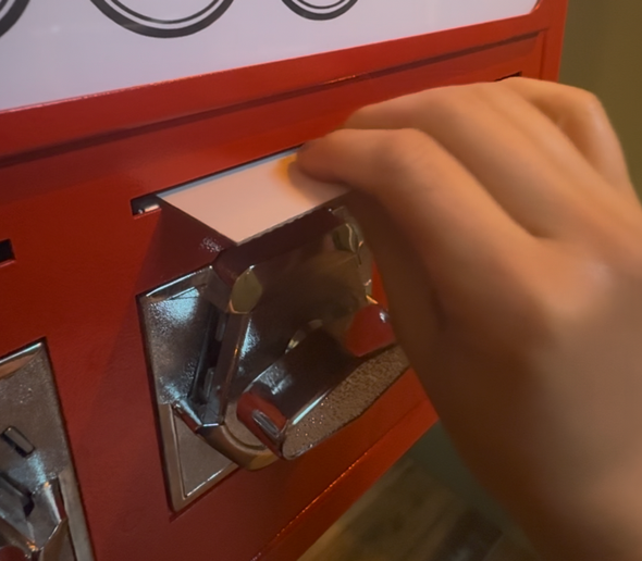 Hand turning a chrome knob on a red vending machine