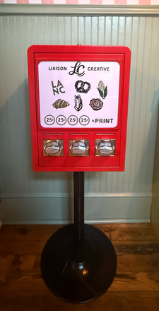 Red cash-recycling kiosk on a black stand in a hallway, with a white sign and three cash slots.