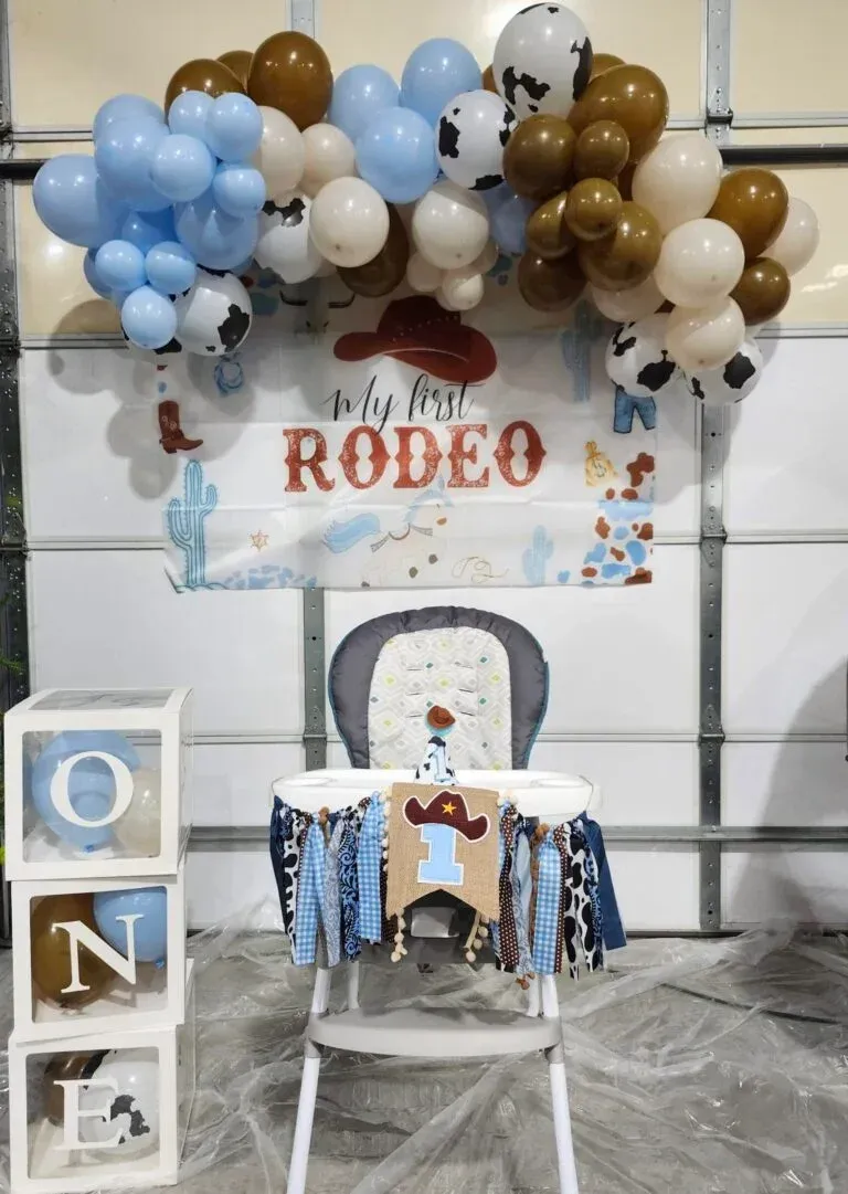 Cowboy-themed first birthday party decorations: balloon arch, banner, decorated high chair,