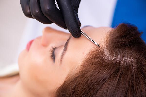 A hair replacement specialist applying treatment to a client's hair while holding a section A hair replacement specialist applying treatment to a client's hair while holding a section