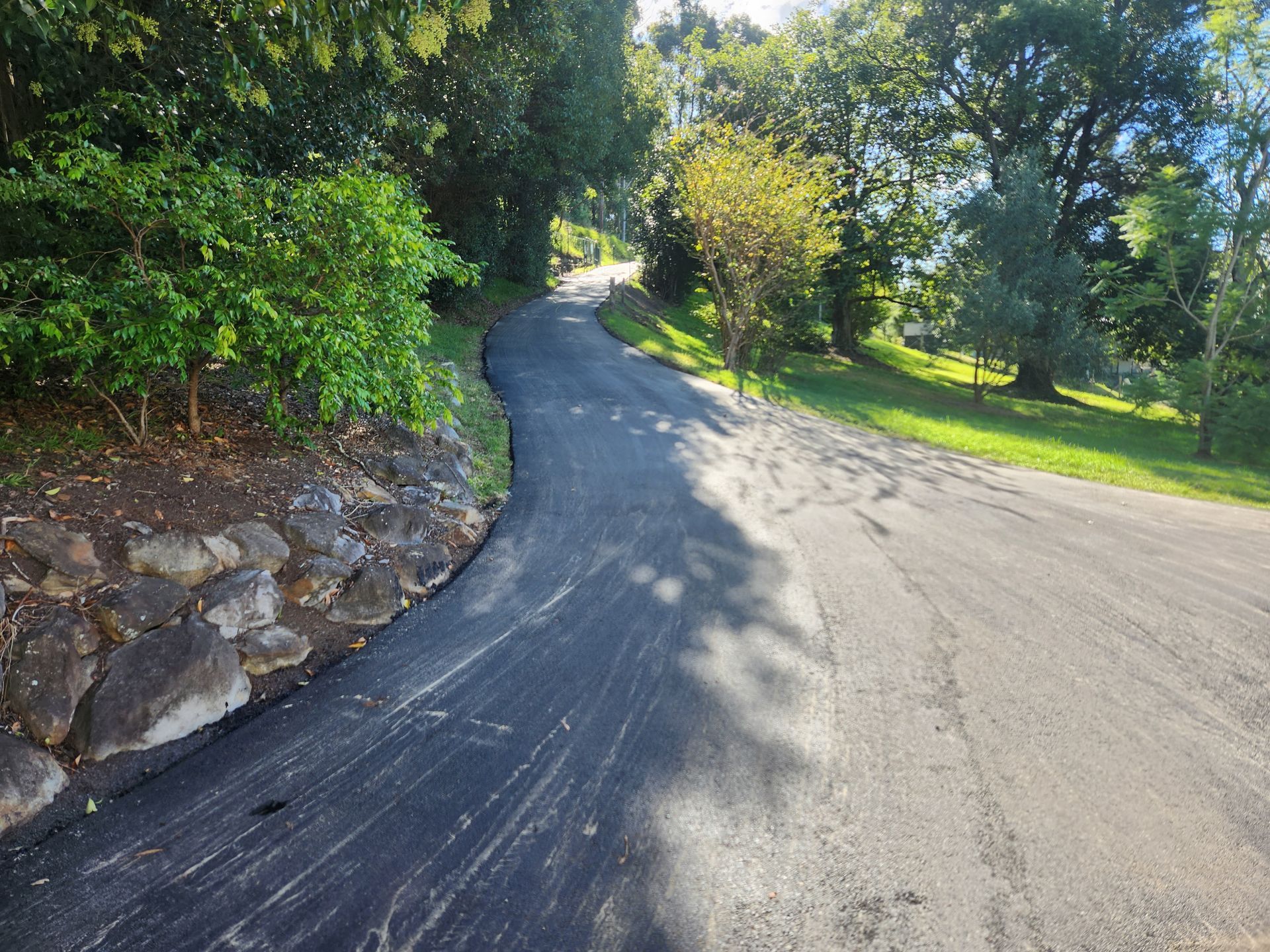 Newly Paved Asphalt Road Curves Up a Hill, Bordered by Green Trees and Grass — TAC Asphalt Services in Warners Bay, NSW