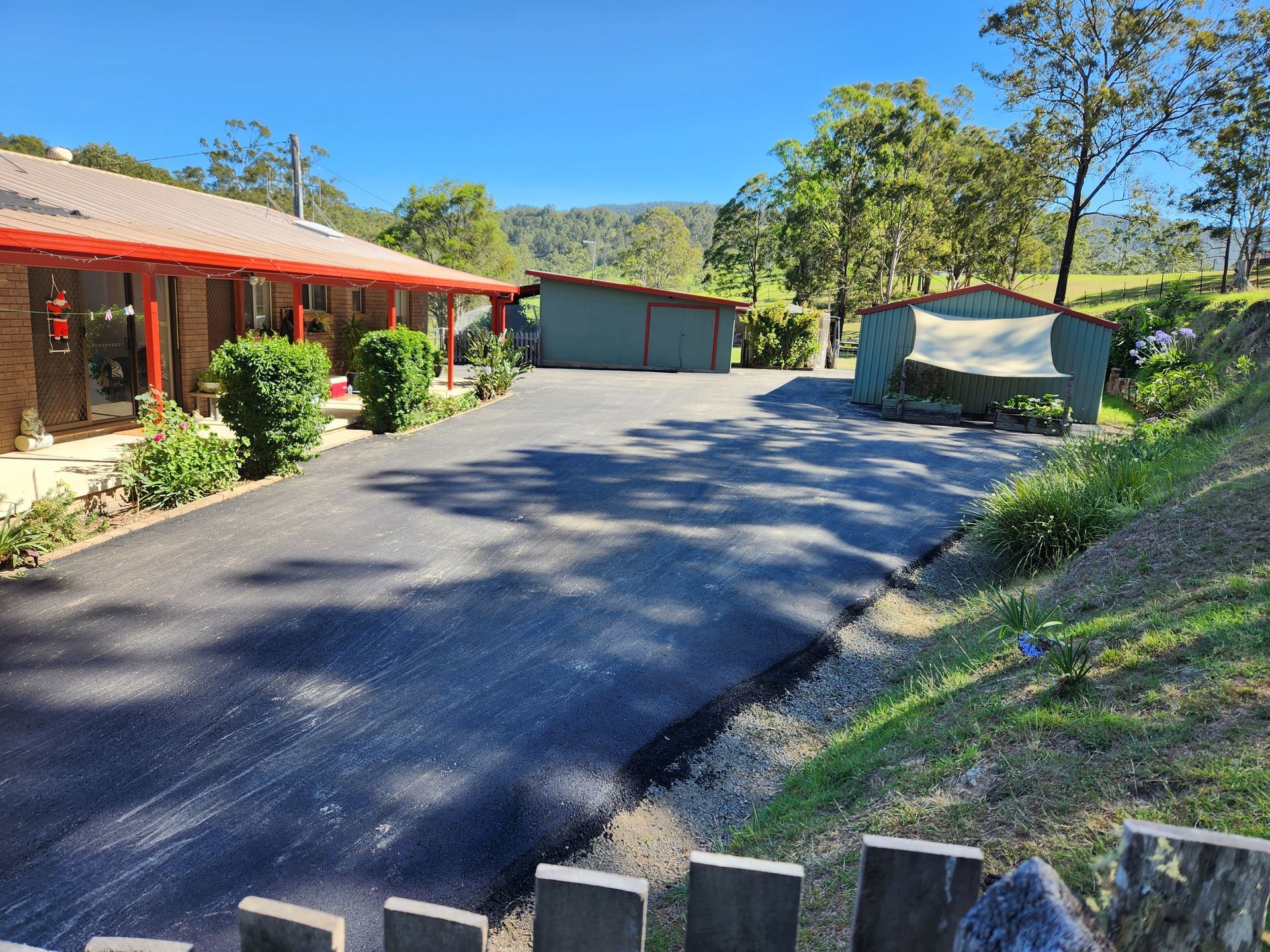 Asphalt Driveway Leading to a Brick House With a Red Roof and Two Green Sheds — TAC Asphalt Services in Port Stephens, NSW