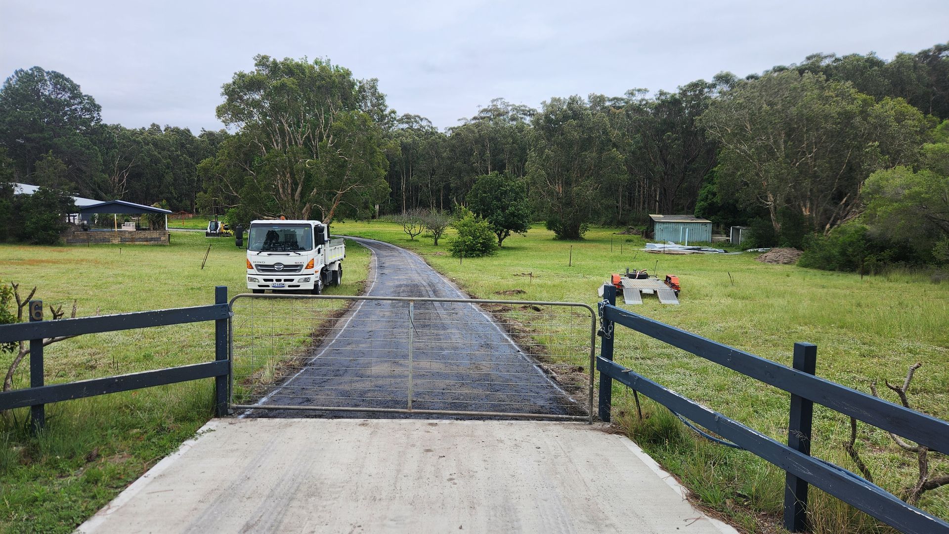 Open Gate Leads to a Driveway With a Truck, Green Field, and Trees — TAC Asphalt Services in Port Stephens, NSW