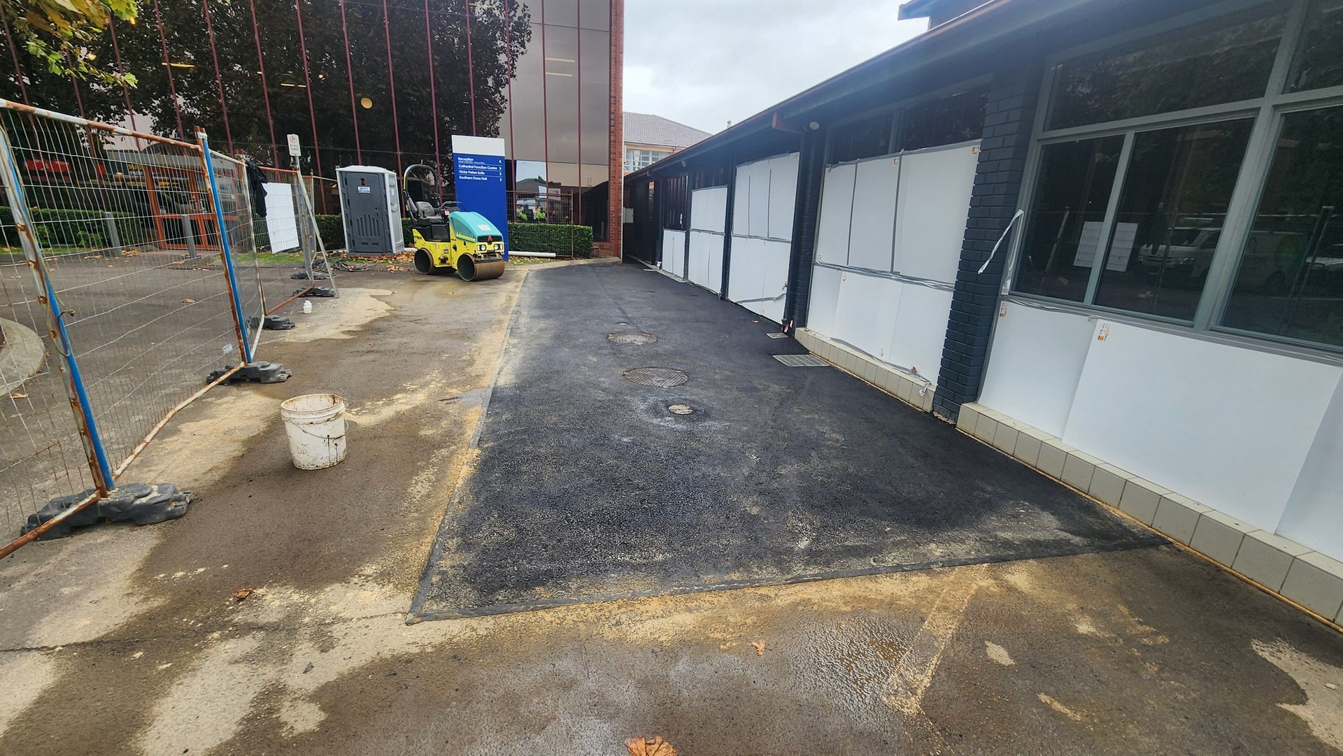 Asphalt Repair On A Sidewalk Beside A Building With White Doors — TAC Asphalt Services in Warners Bay, NSW