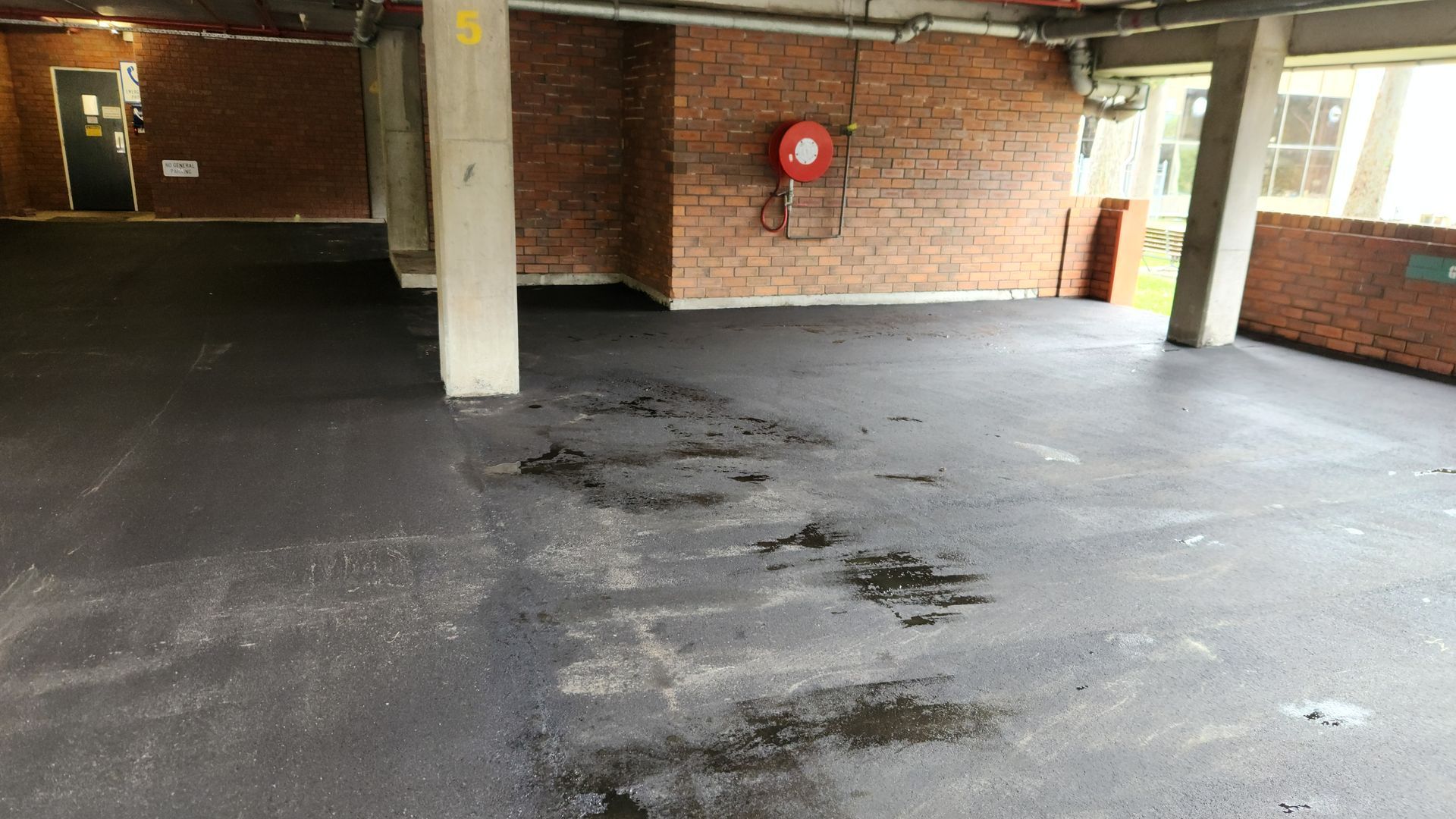 Empty Parking Area With Dark Asphalt Floor, Brick Walls, and Concrete Columns — TAC Asphalt Services in Warners Bay, NSW