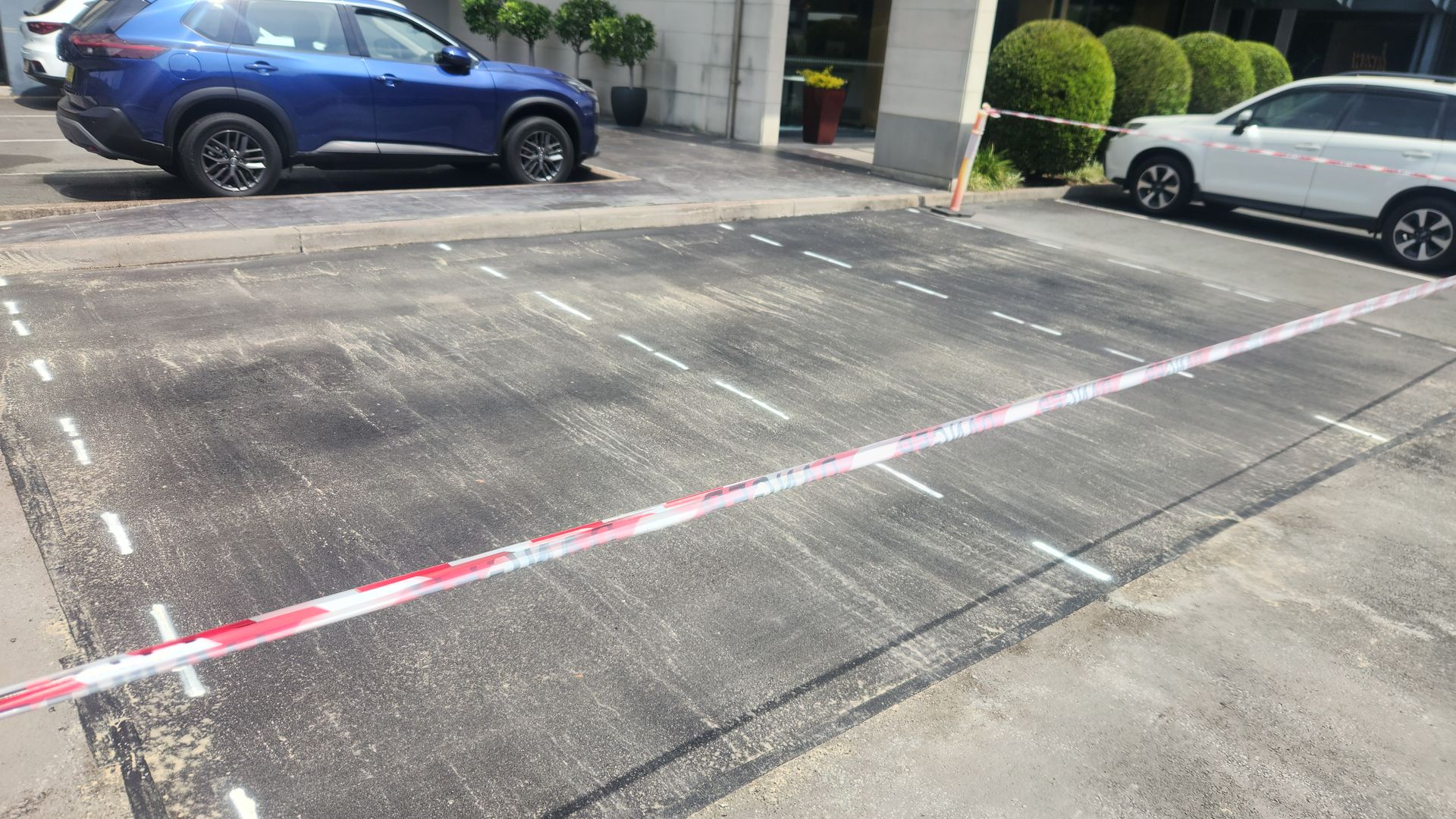 A parking area cordoned off by red and white barrier tape, with two parked cars nearby.