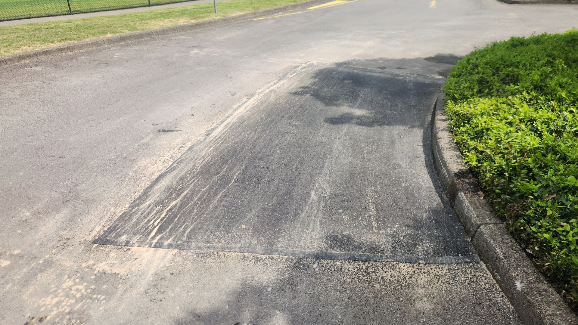 Asphalt Road With a Rectangular Patch Repair. Concrete Curb and Grass on the Right — TAC Asphalt Services in Warners Bay, NSW