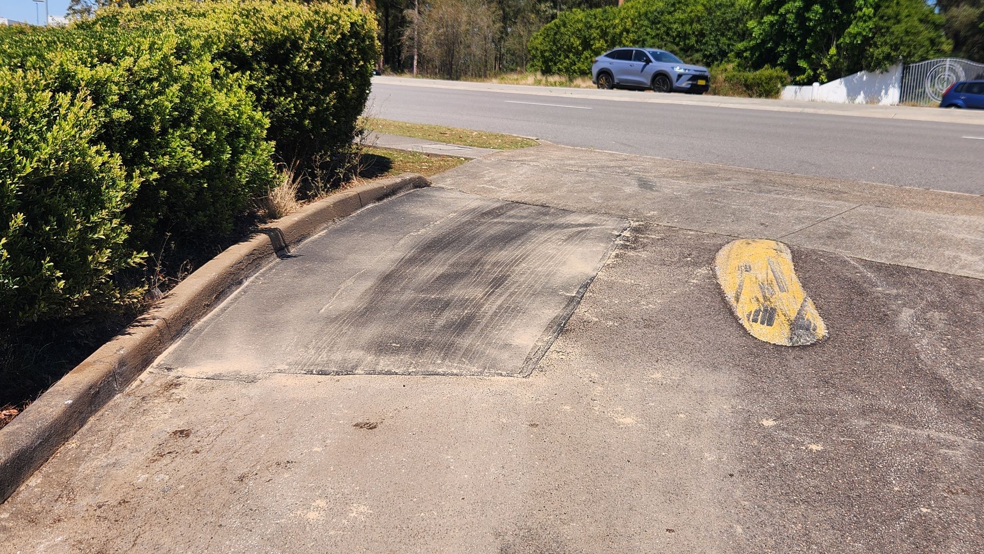 Damaged Asphalt Driveway With a Speed Bump and Road in the Background — TAC Asphalt Services in Warners Bay, NSW
