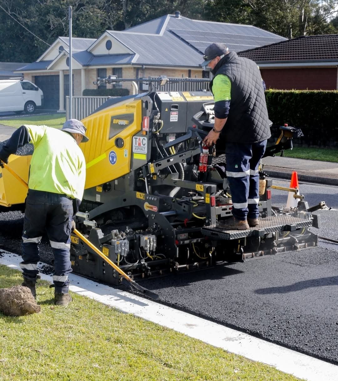 Two Road Workers Paving Asphalt on a Street One Rakes — TAC Asphalt Services in Warners Bay, NSW