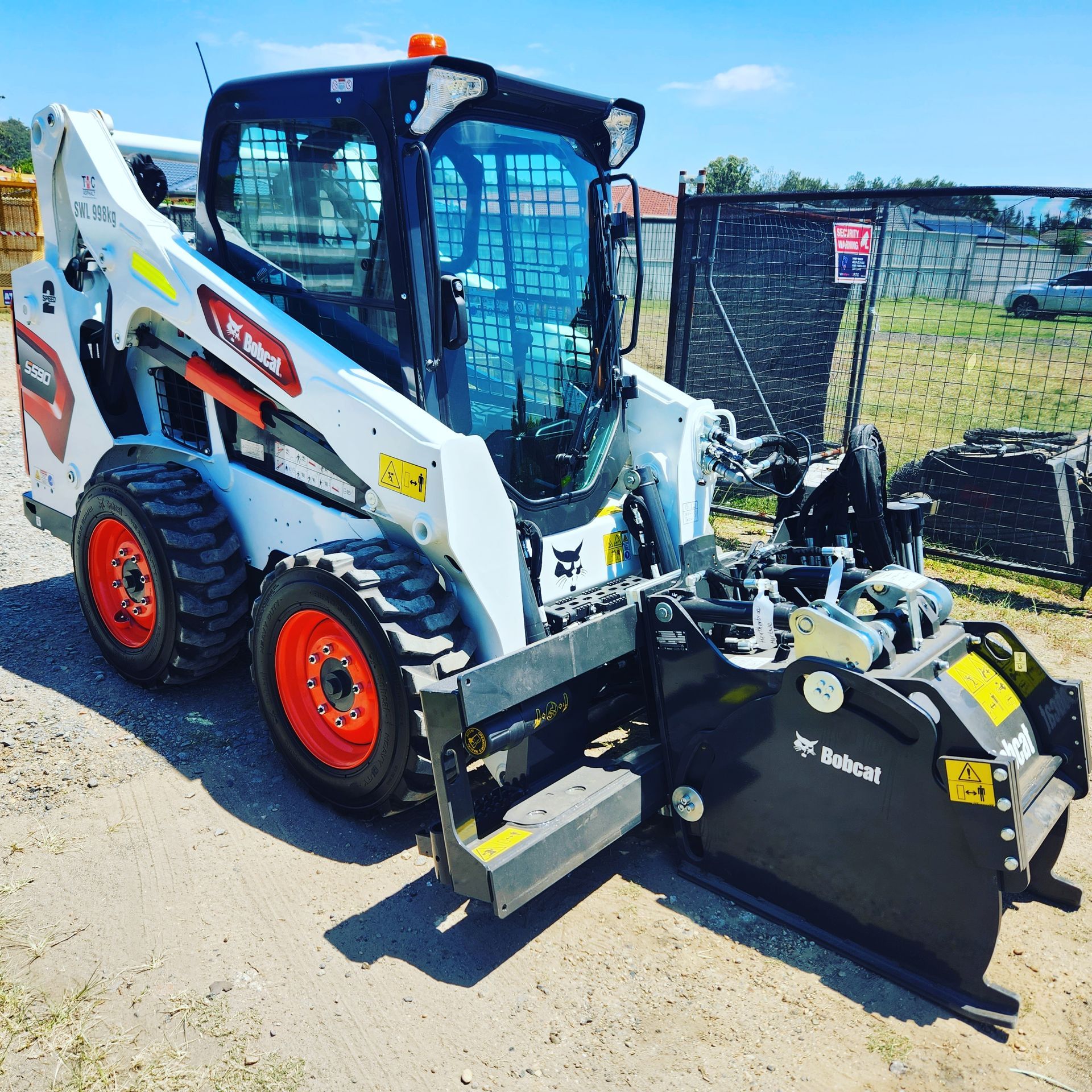 A white Bobcat skid-steer loader with orange wheels, equipped with a front attachment, parked outdoors on a dirt surface.