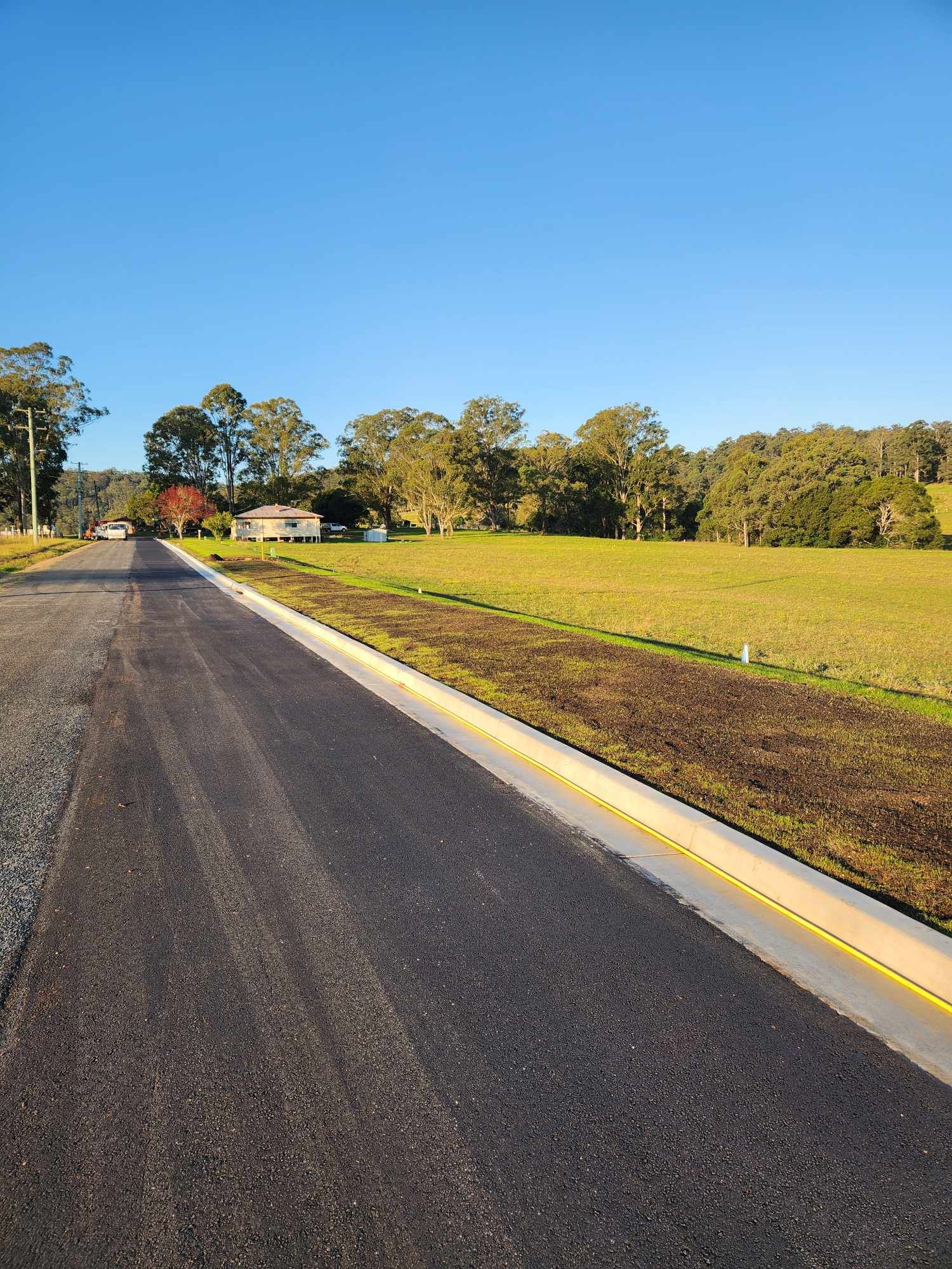 Asphalt Road Bordered by Concrete, Grassy Field, and Trees Under a Clear Blue Sky — TAC Asphalt Services in Warners Bay, NSW