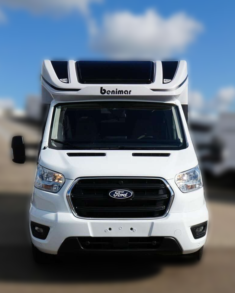 Witte Ford campervan met zwarte accenten, geparkeerd onder een blauwe hemel met wolken.