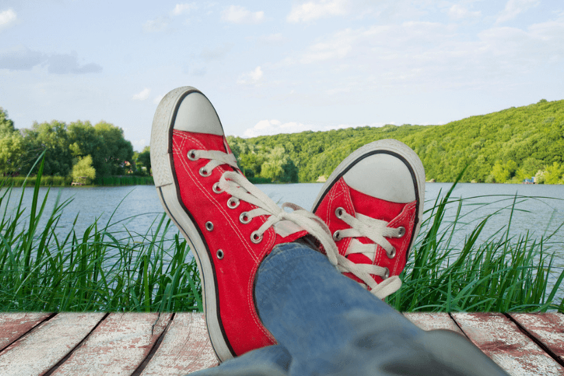 Rode sneakers aan, benen gekruist, ontspannen zittend op een steiger met uitzicht op een meer.
