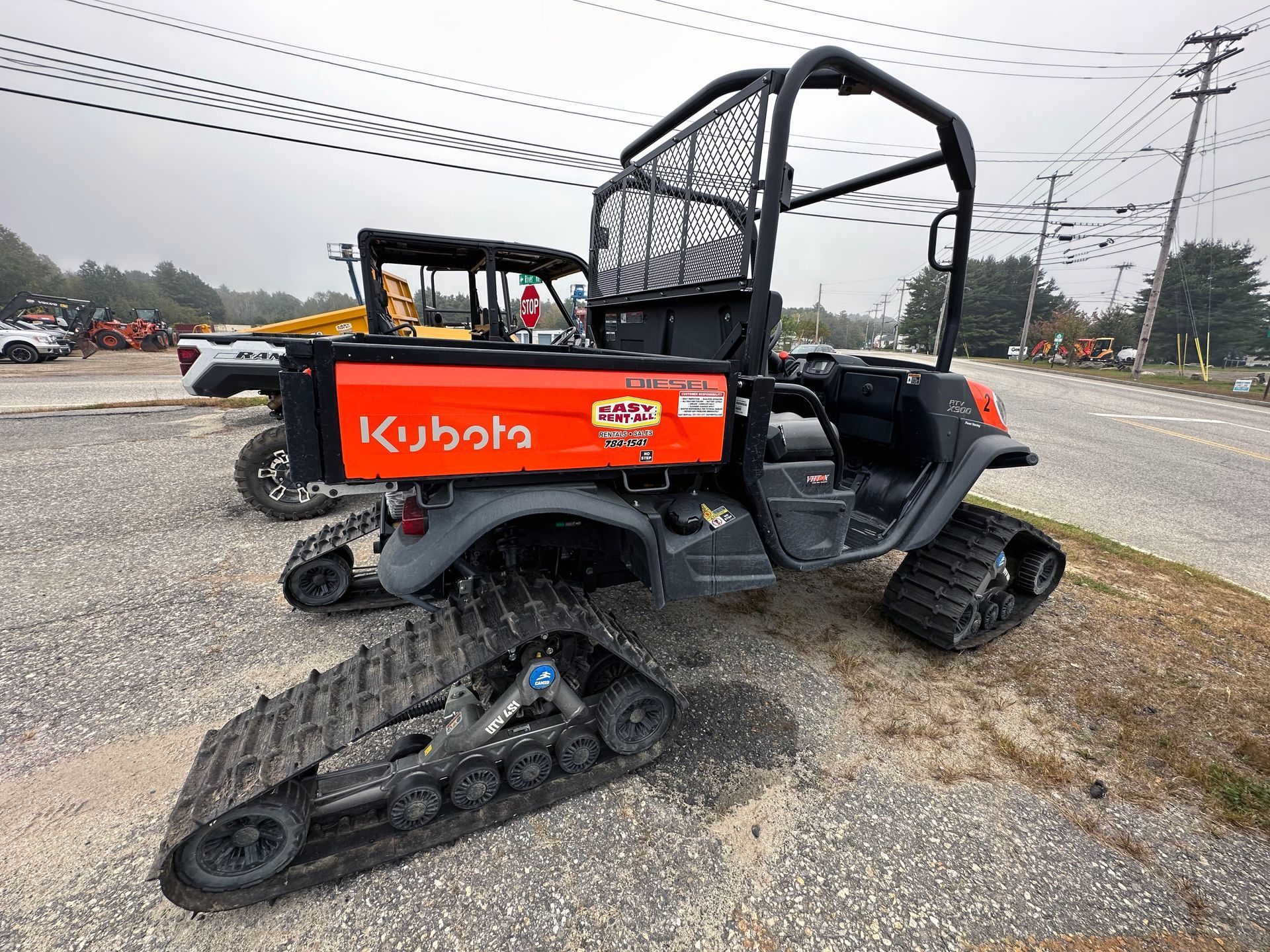 A kubota utility vehicle with tracks is parked on the side of the road.