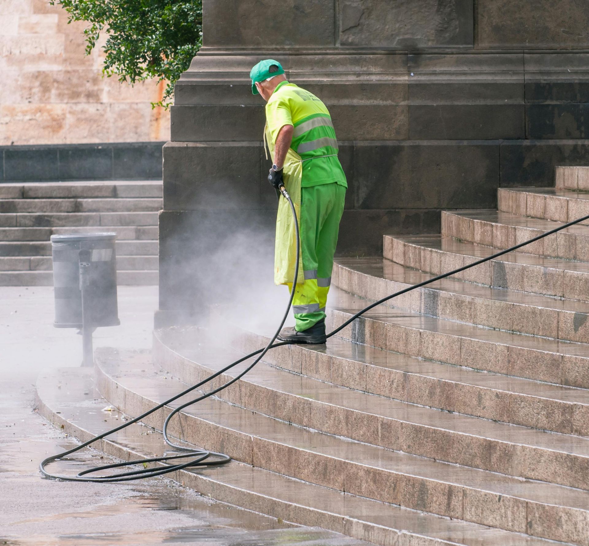 A person in green safety gear power washes stone steps outdoors.