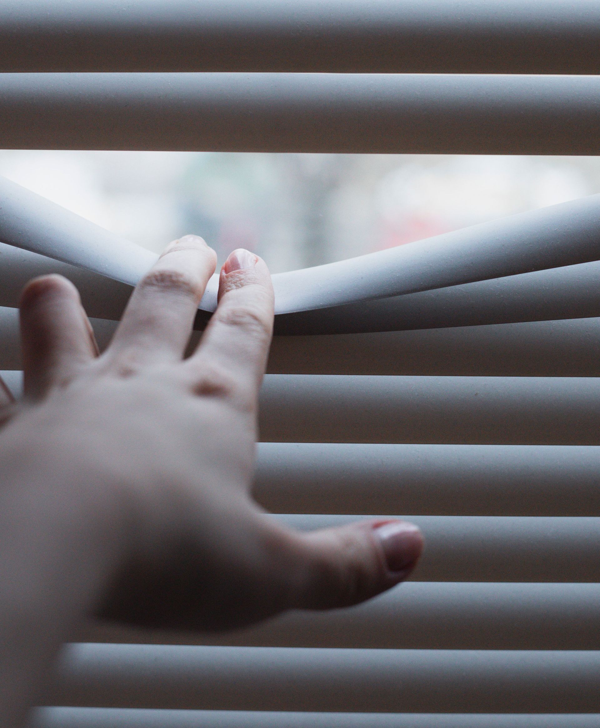 Hand reaching through white blinds with a small gap of daylight behind them