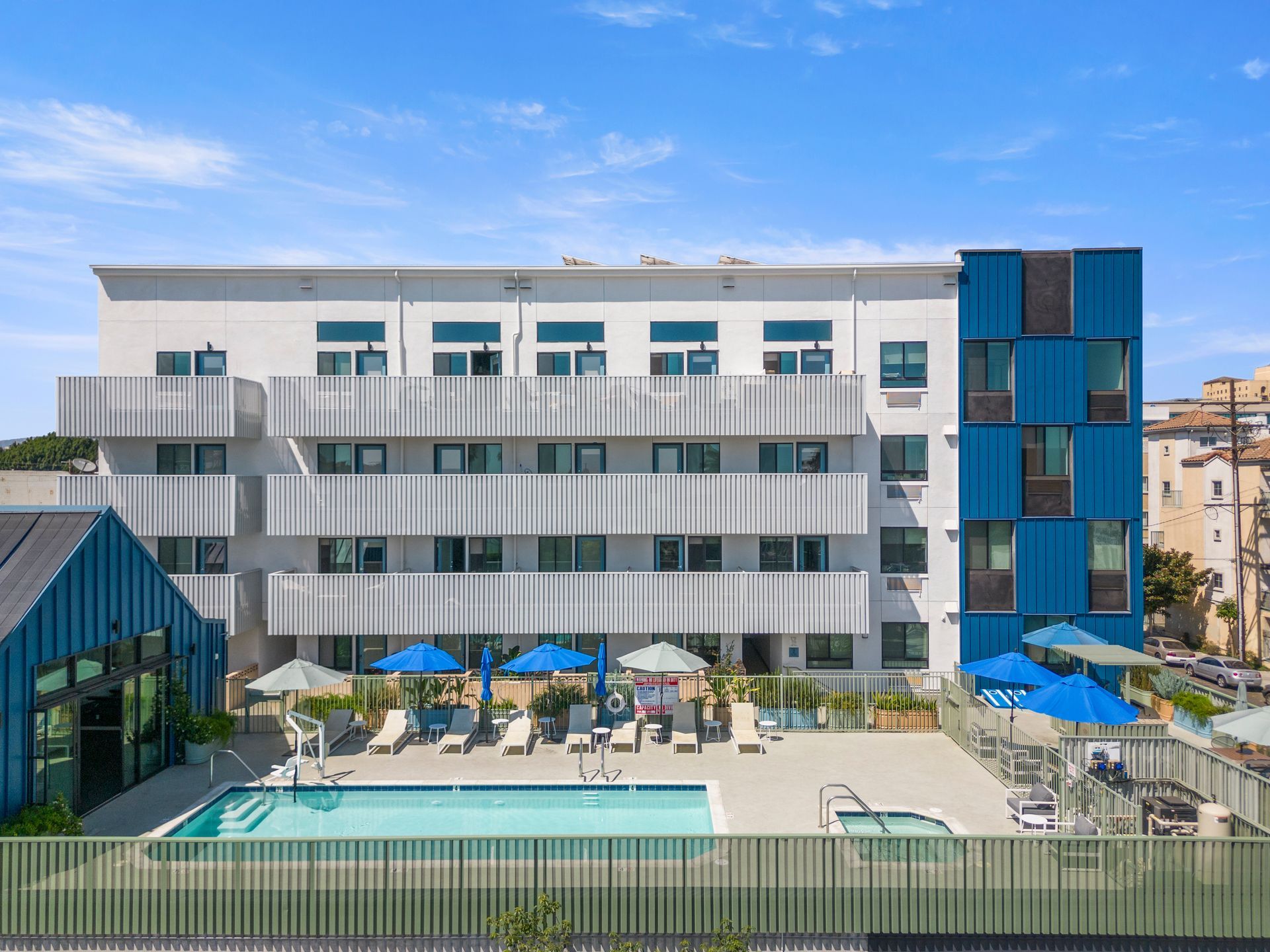 4Mica  aerial view of a large apartment building with a large swimming pool in front of it.