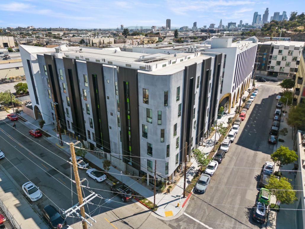 Aerial view of a modern white apartment building on a city street, with a skyline in the distance.
