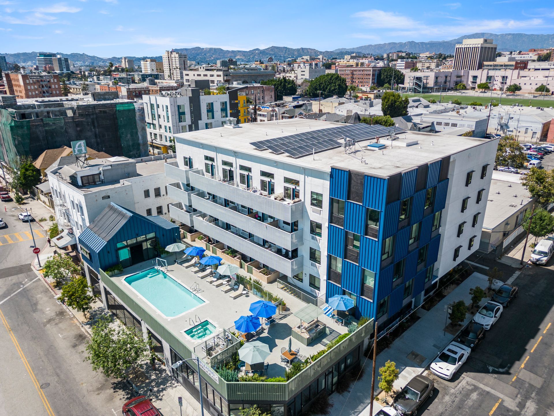 4Mica  aerial view of a large building with a swimming pool in front of it.