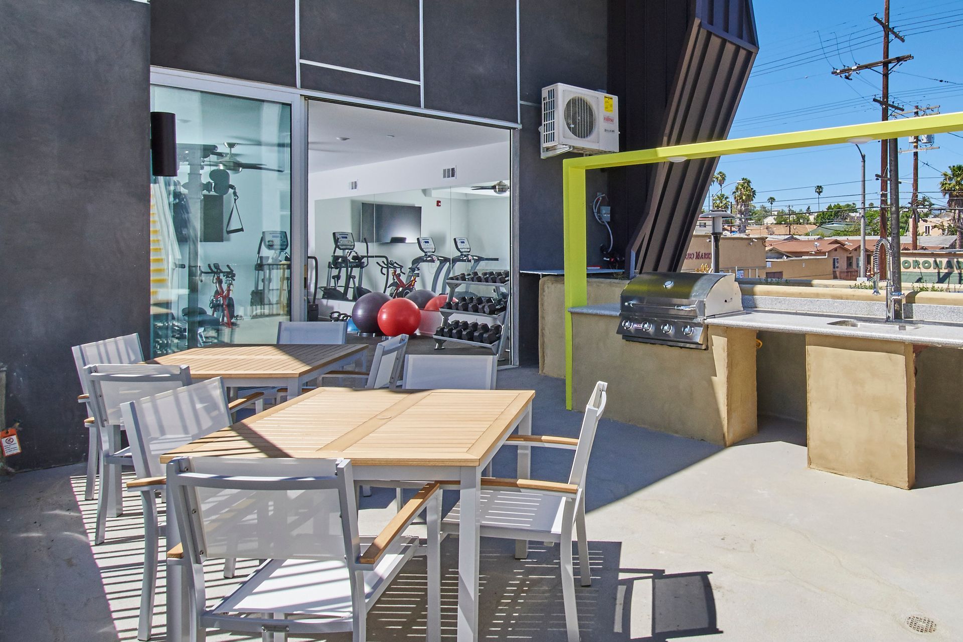 Outdoor patio with tables and chairs, a grill, and a gym visible through a glass door.