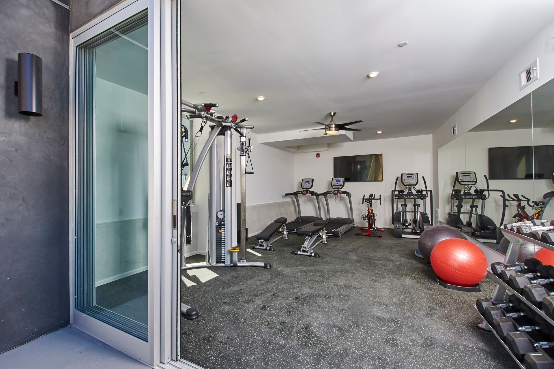Gym interior with exercise equipment including treadmills, weights, and a multi-station machine.