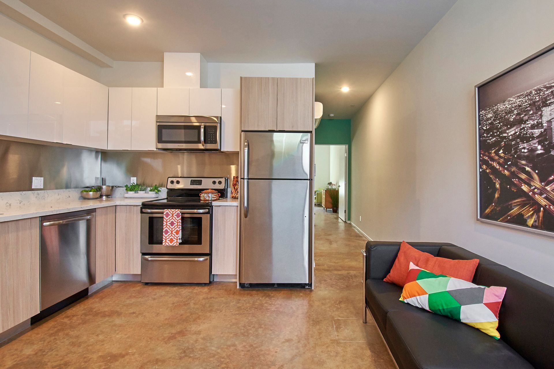 A living room with a couch and a kitchen with stainless steel appliances