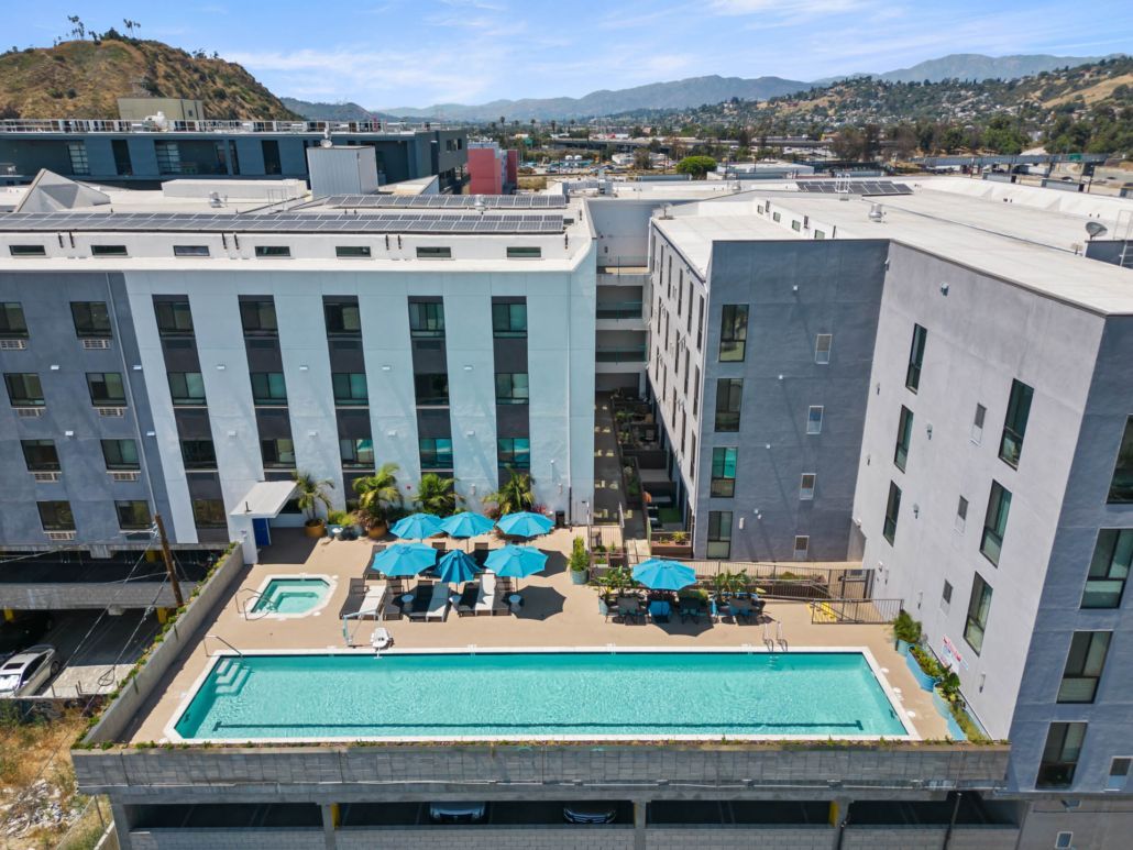 Modern apartment complex with a rooftop pool, turquoise umbrellas, and mountain views