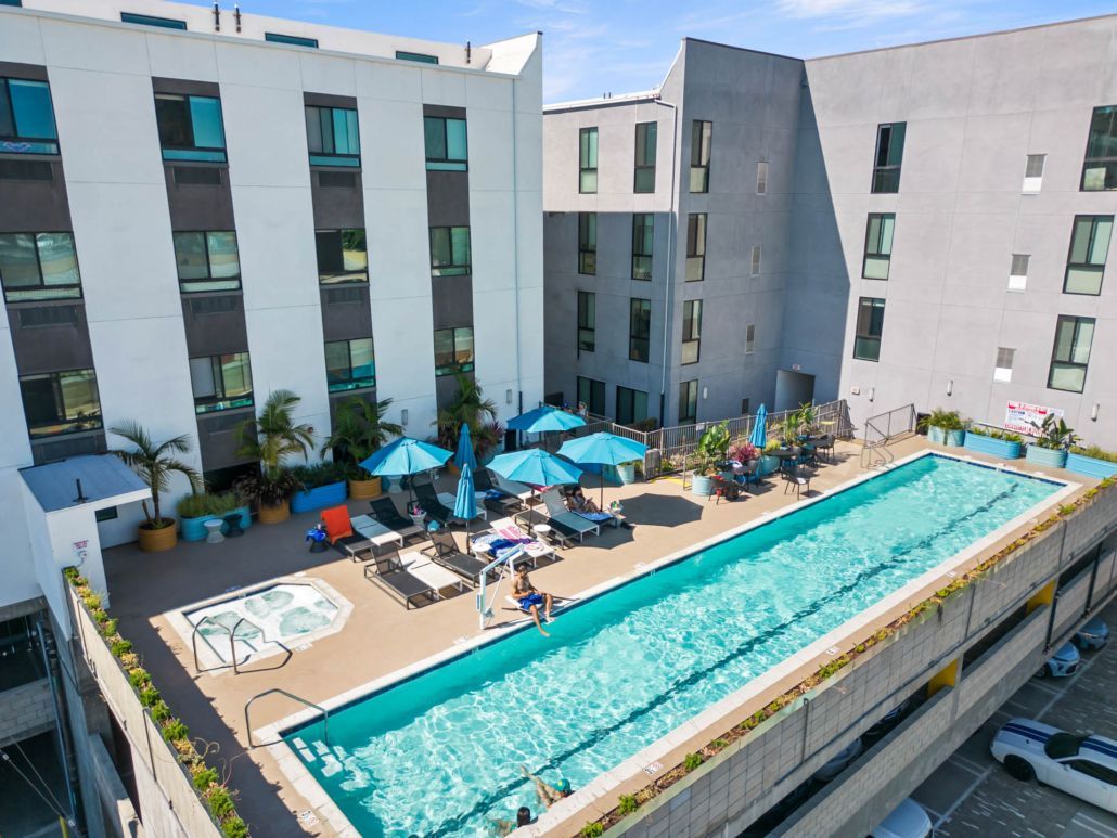 Modern hotel courtyard with a rectangular pool, blue umbrellas, lounge chairs, and surrounding rooms