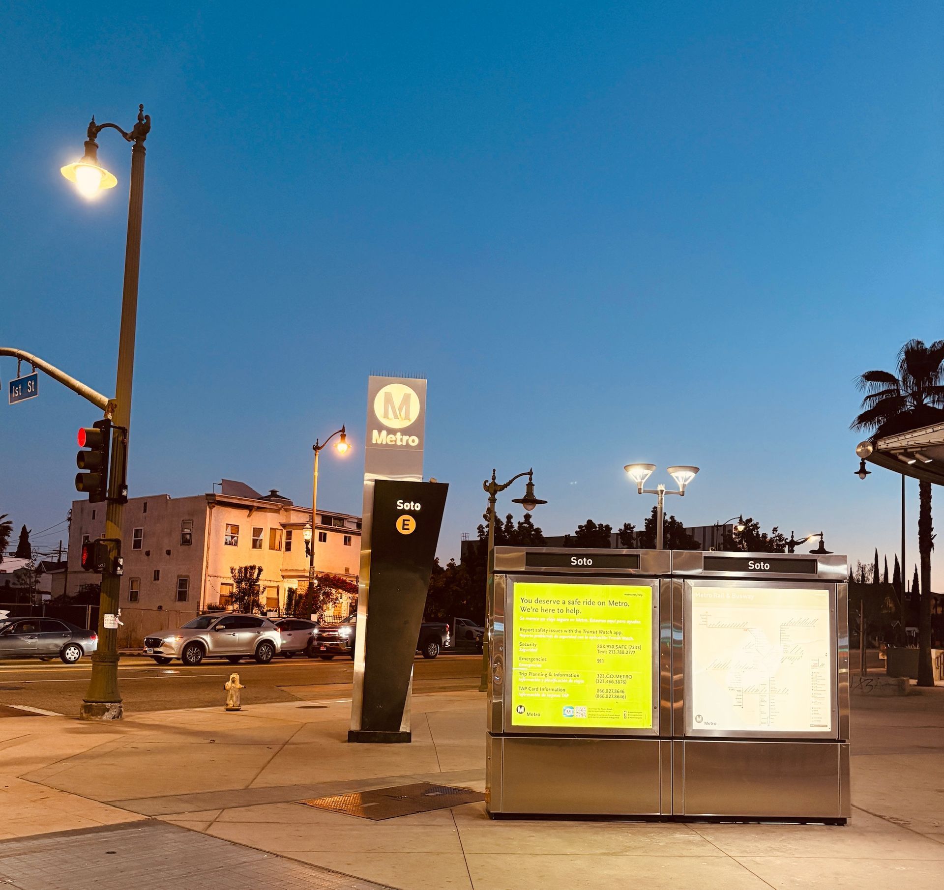 Metro train station at dusk, featuring a schedule, signage, and streetlights.