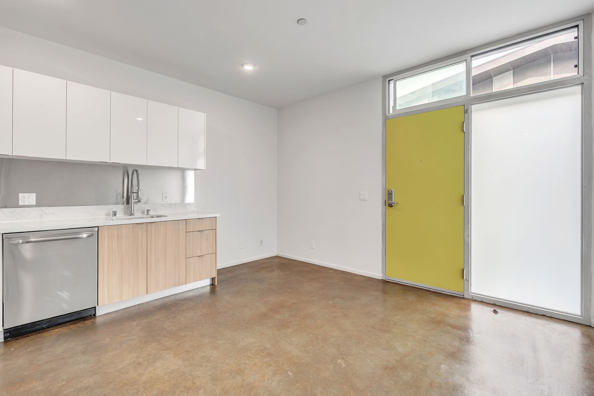 A small modern kitchen with white cabinets, light wood drawers, and a yellow door.