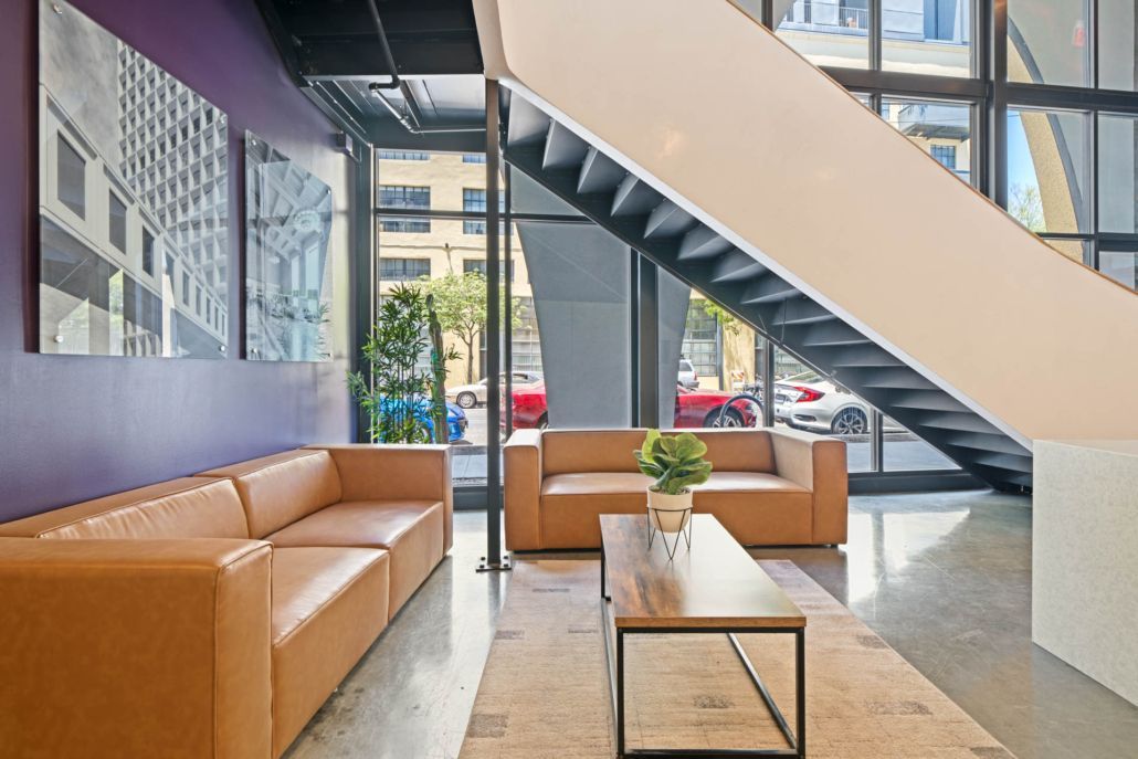 Modern lobby with tan sofas, staircase, coffee table, and large windows