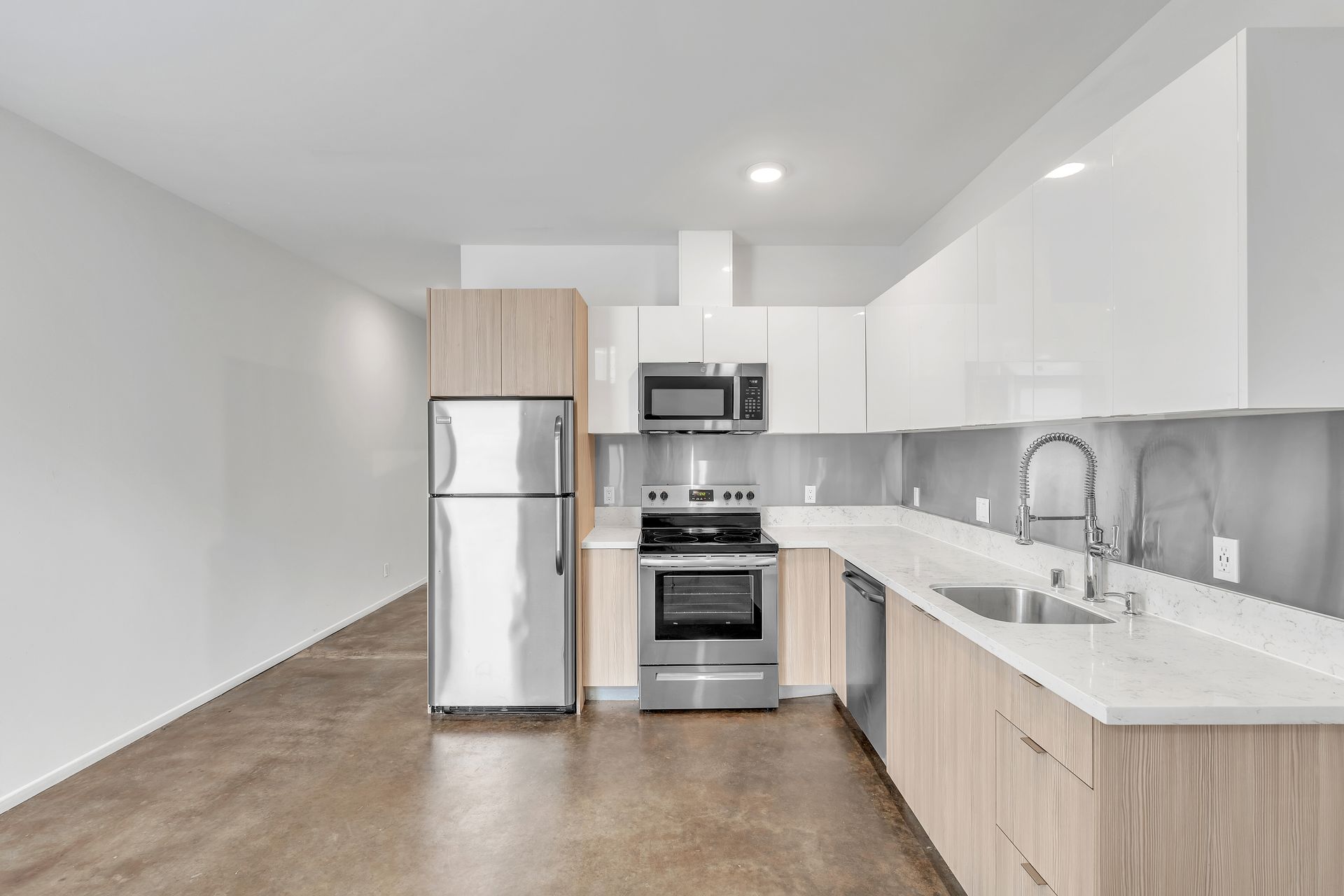 Modern kitchen with stainless steel appliances, light wood cabinets, and white countertops.
