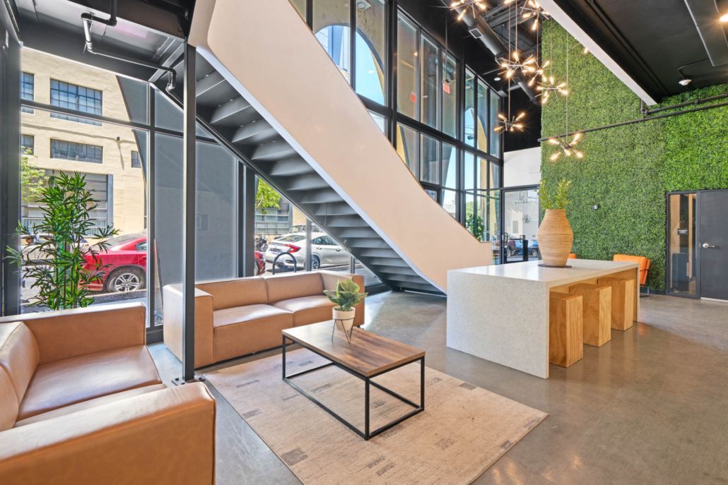 Modern lobby with staircase, wood benches, glass walls, and a green living wall