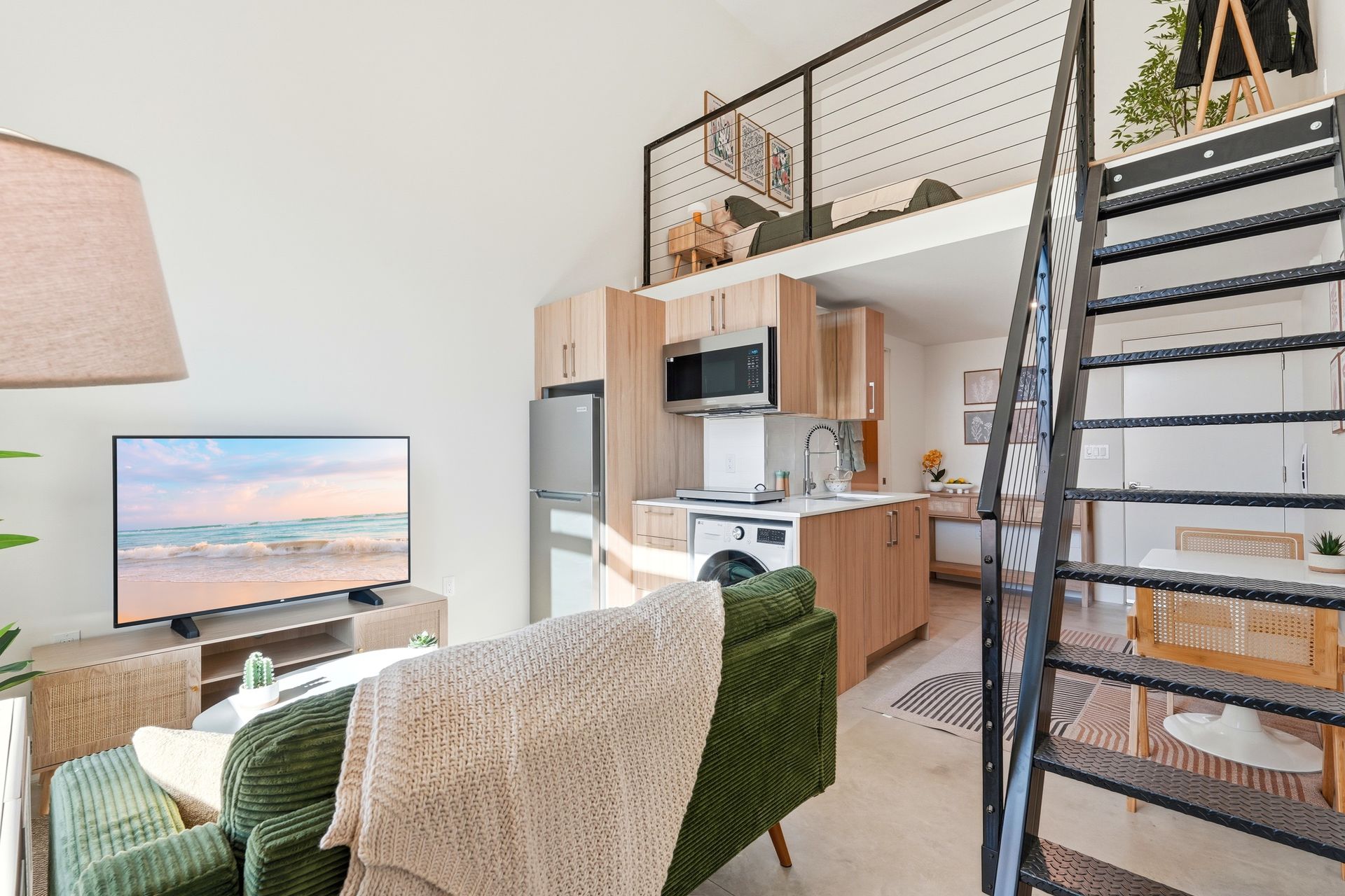 Small studio apartment with a loft bed, kitchen, and living area with a television.