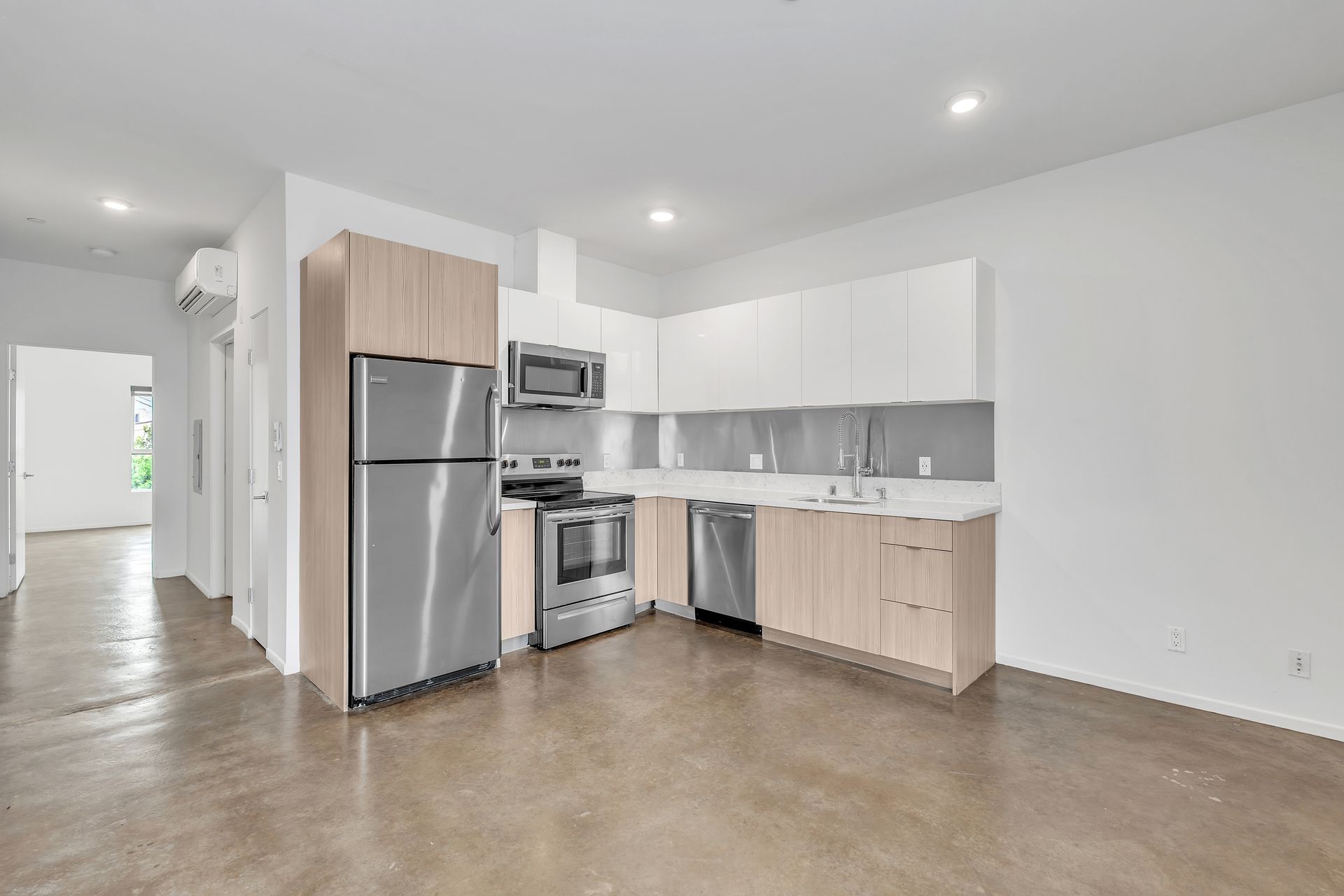 Modern kitchen with stainless steel appliances, light wood cabinets, and white walls.