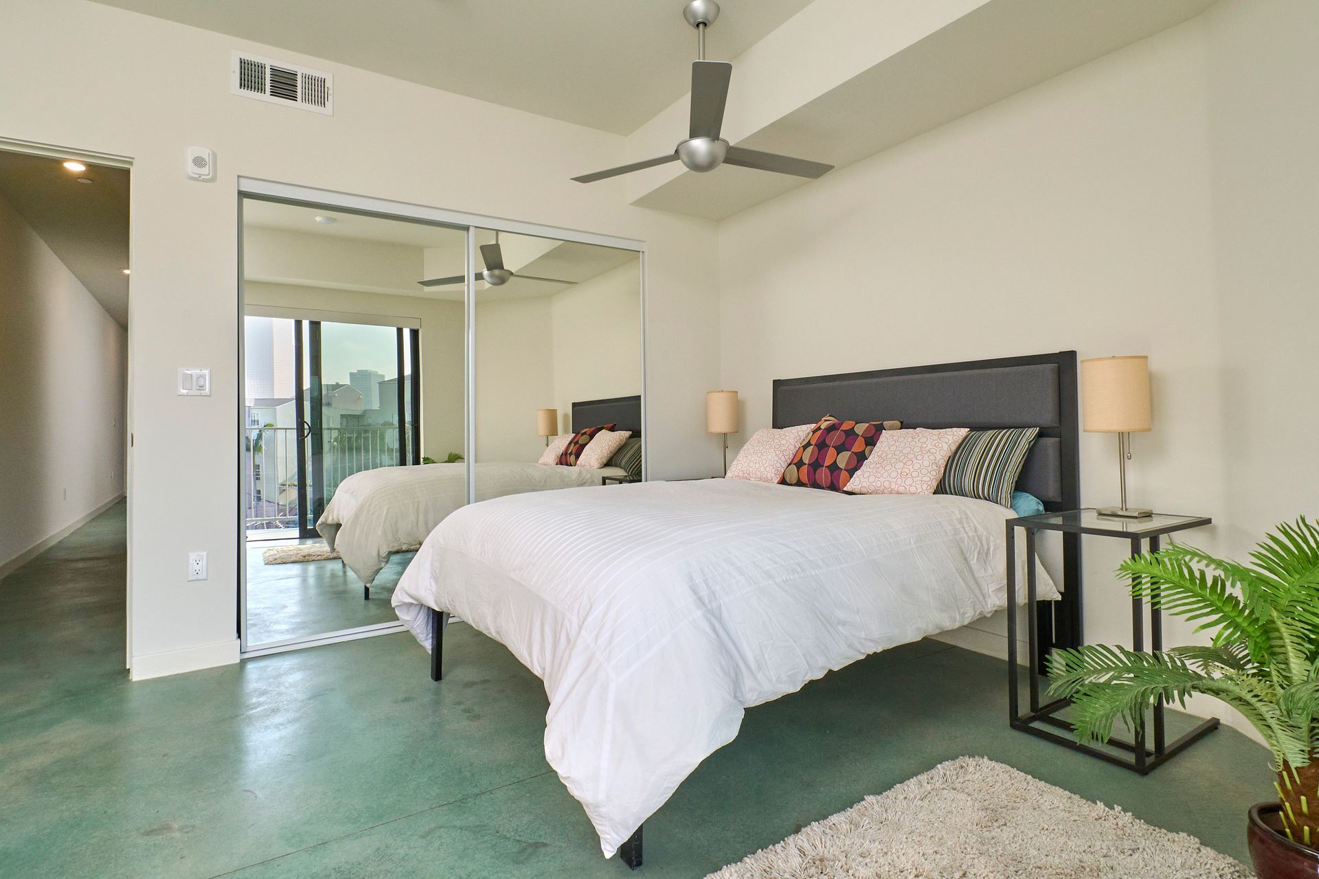 Modern bedroom with two white beds, mirrored closet, ceiling fan, and sliding glass doors opening to a balcony