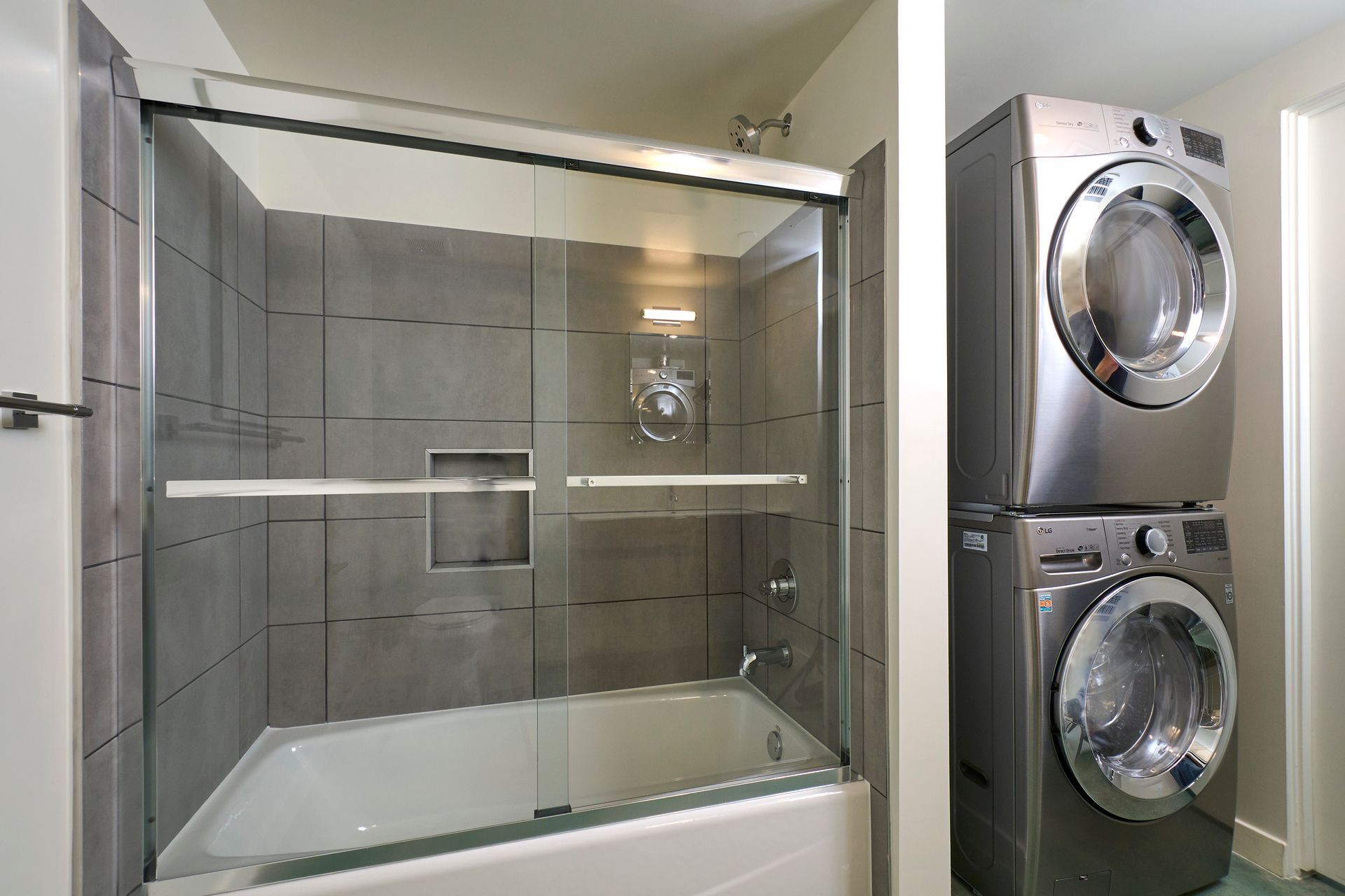 Glass shower next to stacked washer and dryer in a modern bathroom
