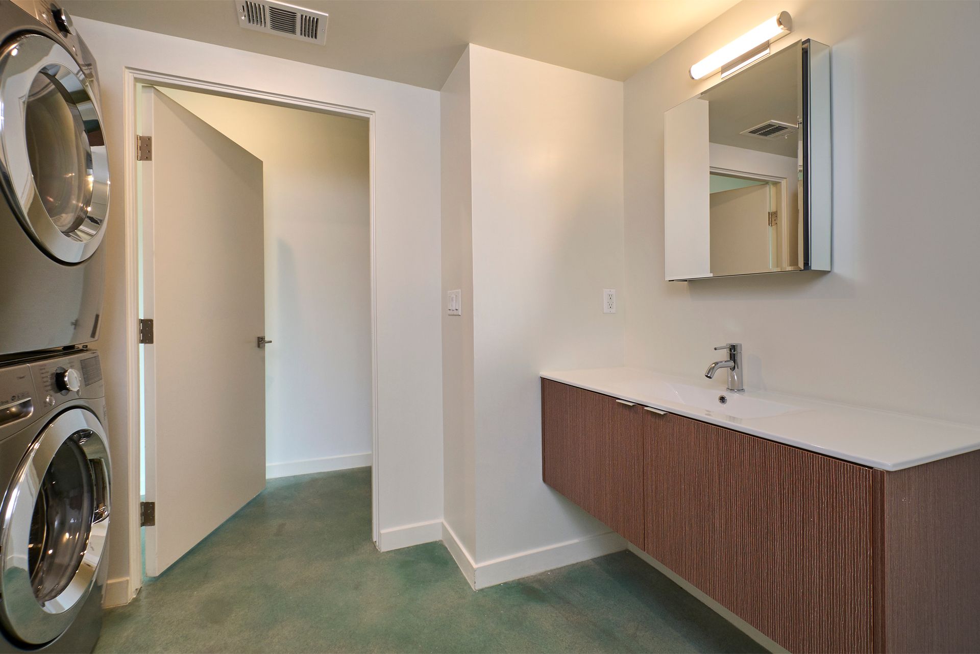 Laundry room with stacked washer and dryer, open doorway, and vanity sink with mirror.
