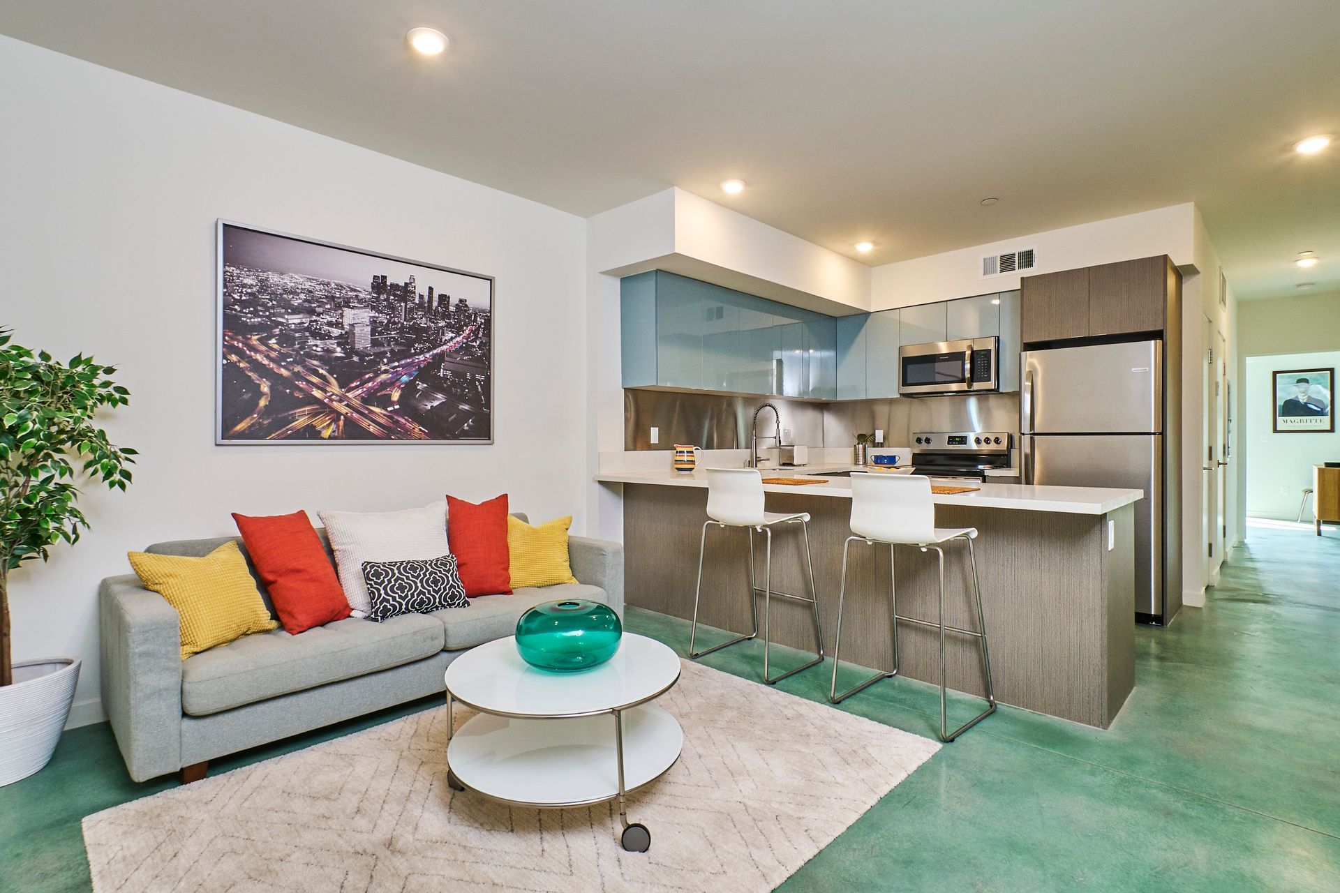 Modern living room and kitchen with gray sofa, colorful pillows, round coffee table, and stainless steel appliances
