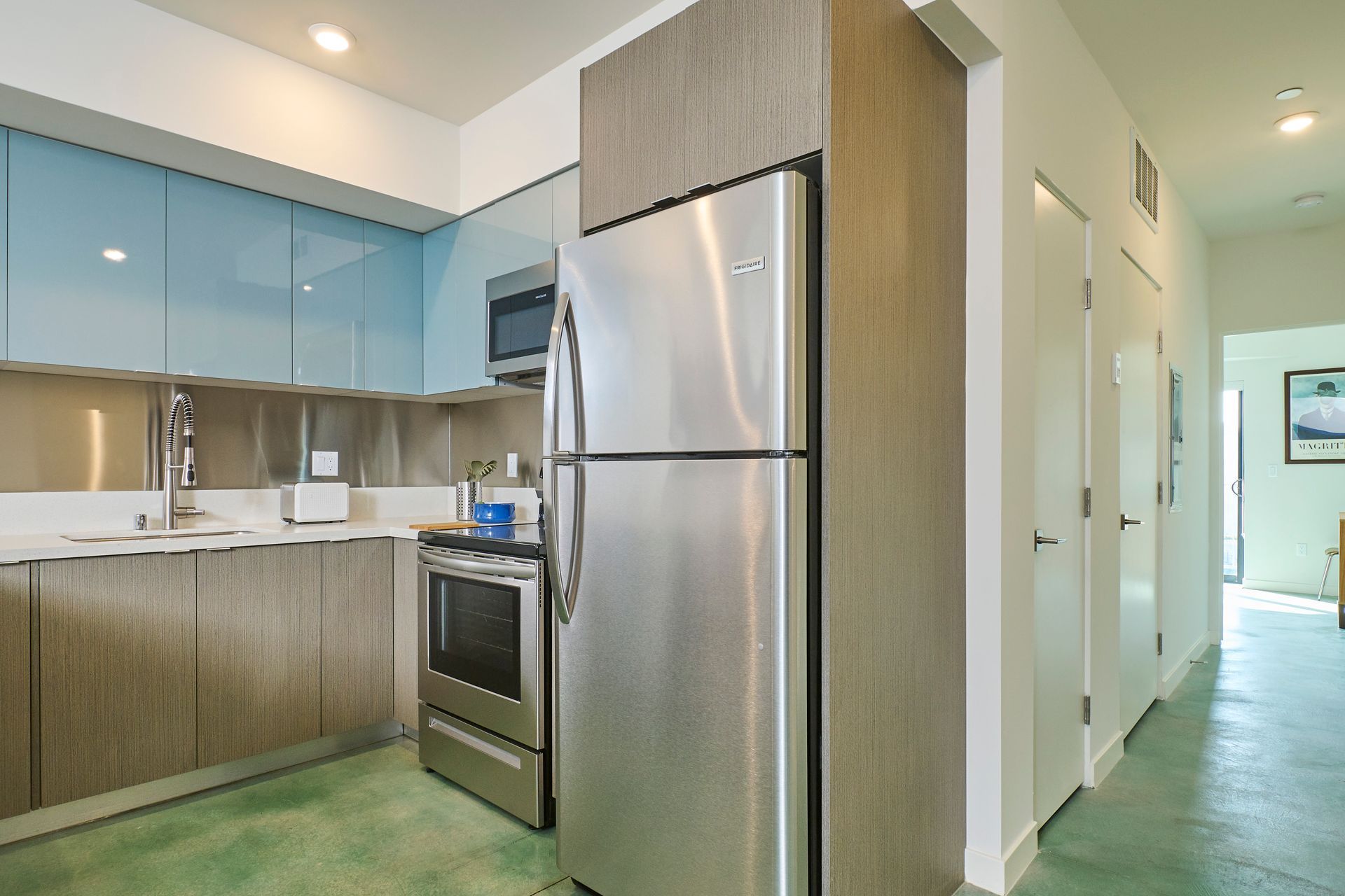 Modern kitchen with stainless steel appliances, blue cabinets, and a hallway to the right