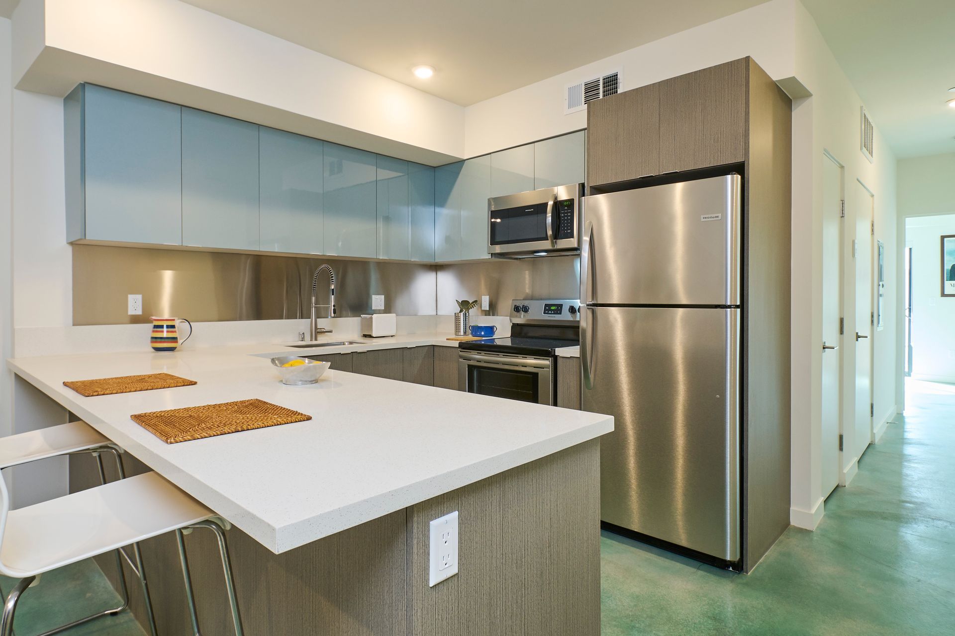 Modern kitchen with white island, light wood cabinets, and stainless steel refrigerator and appliances