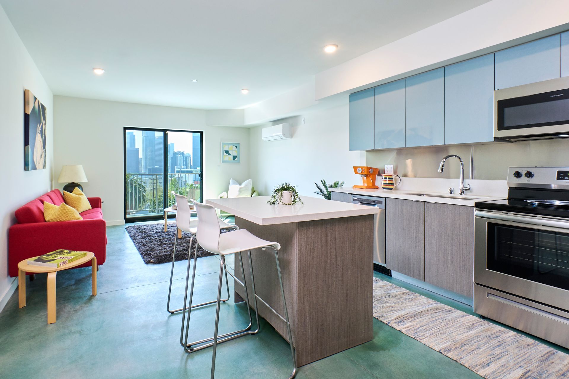 Bright modern kitchen with island, stainless appliances, teal floor, and red sofa by sliding glass doors