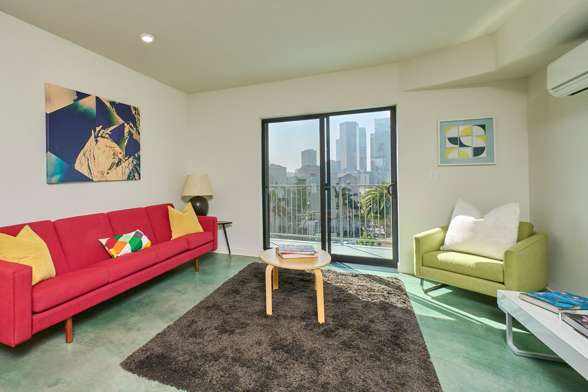Bright living room with red sofa, green chair, coffee table, and city-view balcony doors