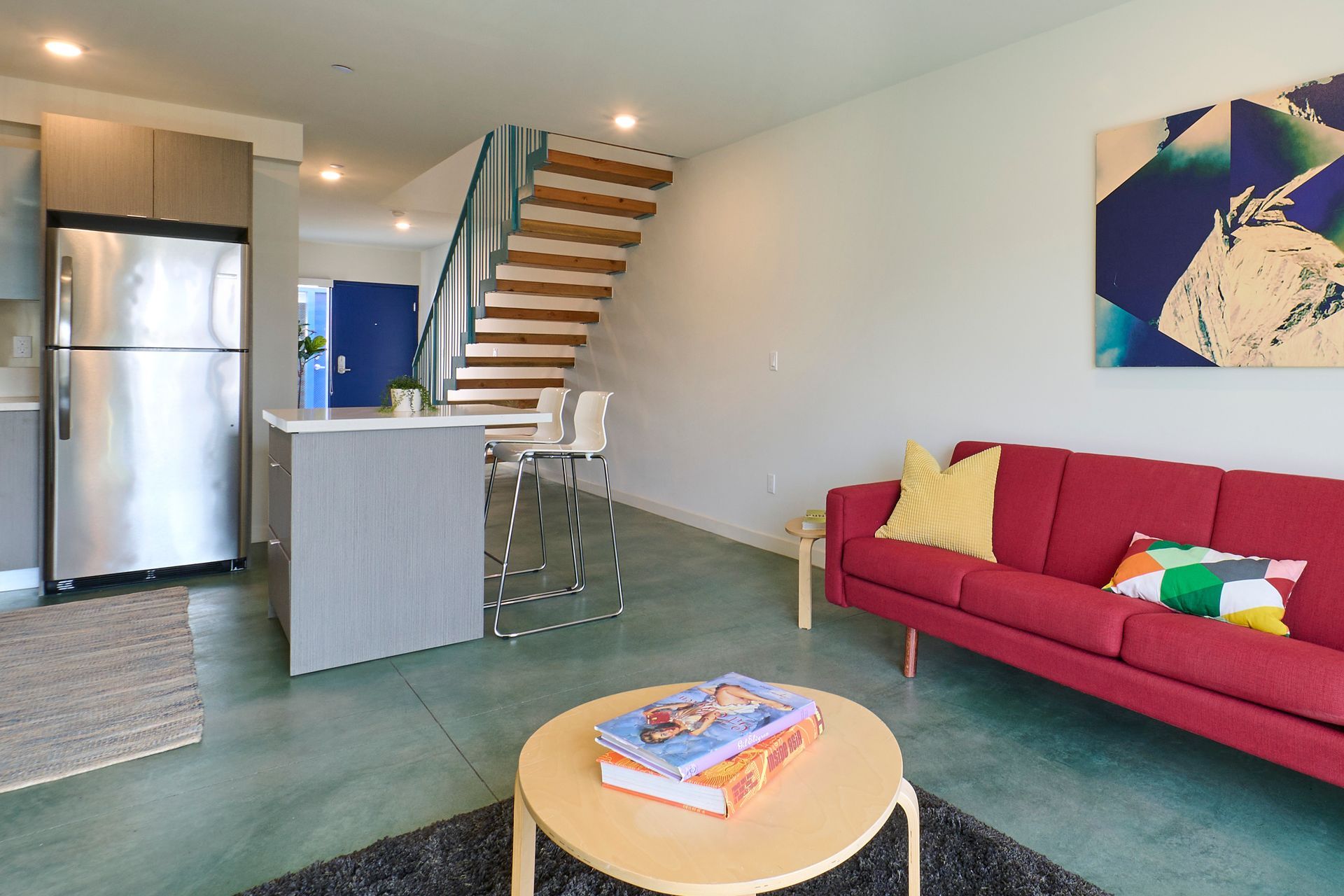 Modern living room with red sofa, coffee table, staircase, and stainless steel kitchen appliances