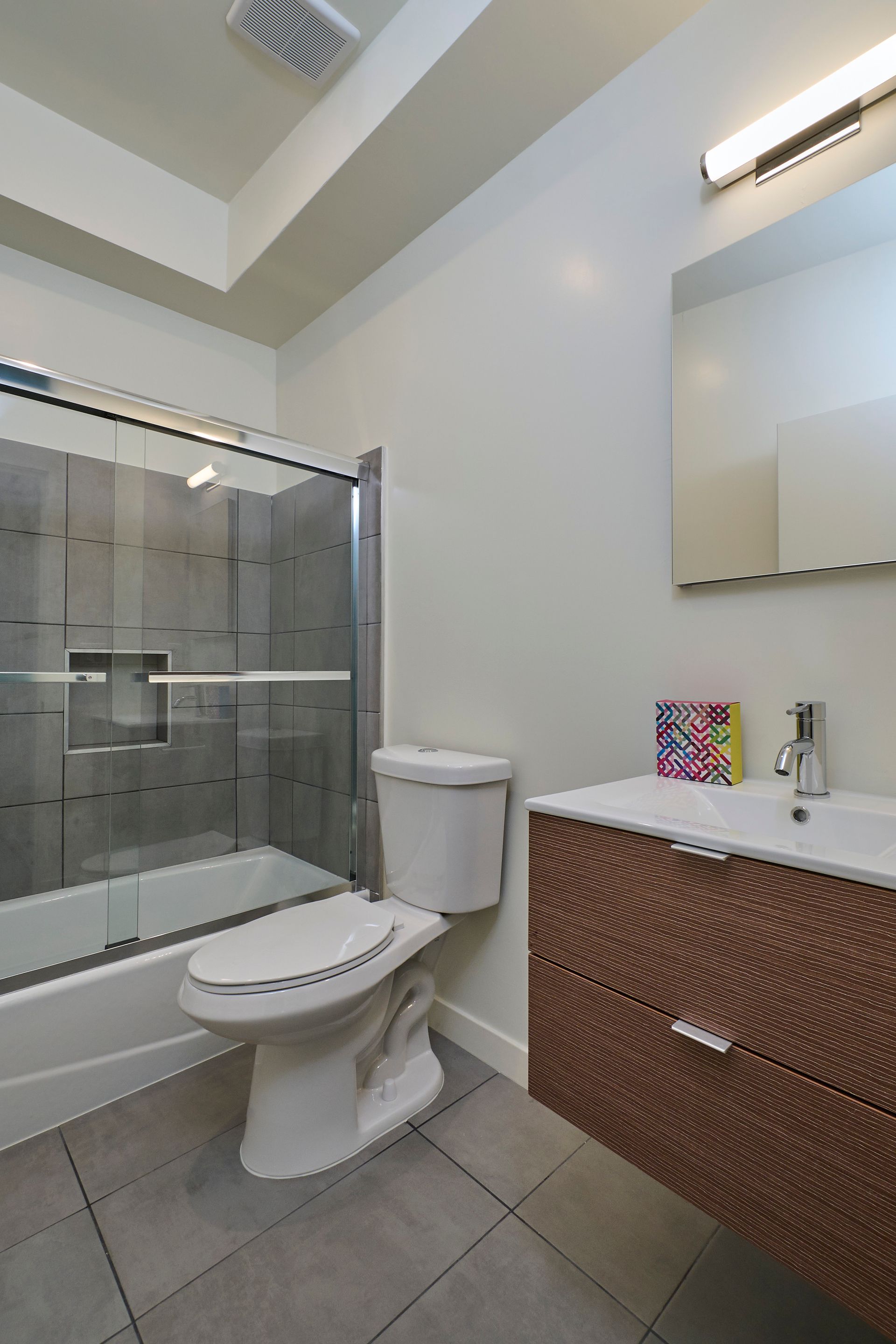 Bathroom with toilet, glass shower, and brown vanity with sink and mirror.