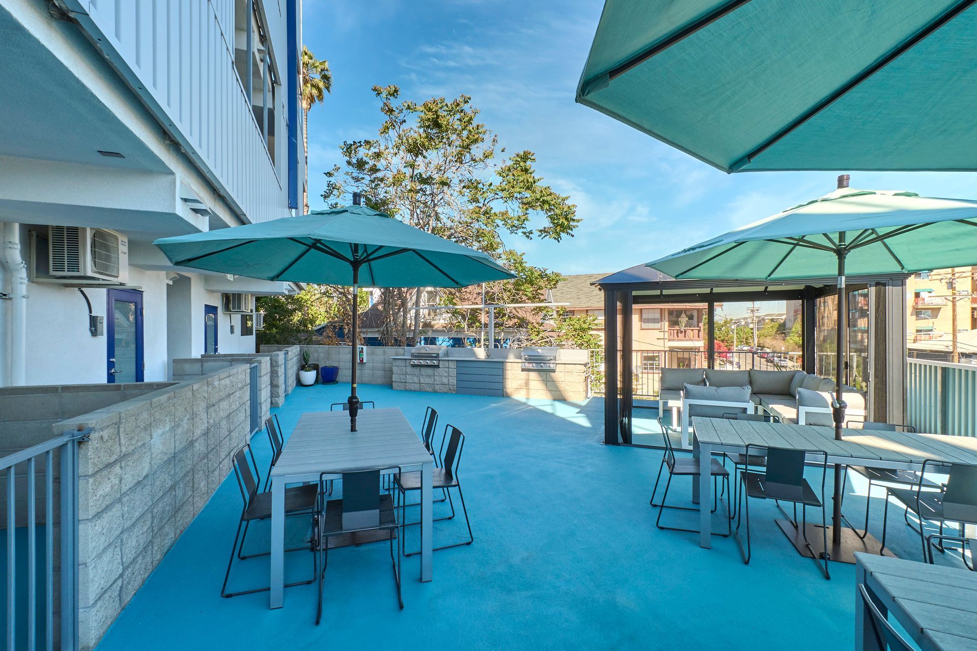 Outdoor patio with teal tables and umbrellas beside a modern building, overlooking the water