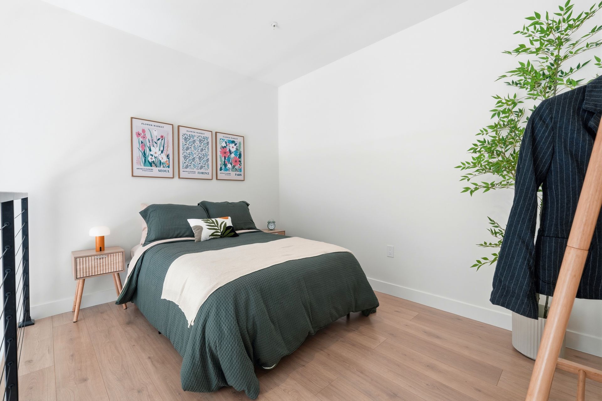 Bedroom with bed, art, small table, and ladder rack holding a jacket, on light wood floor.